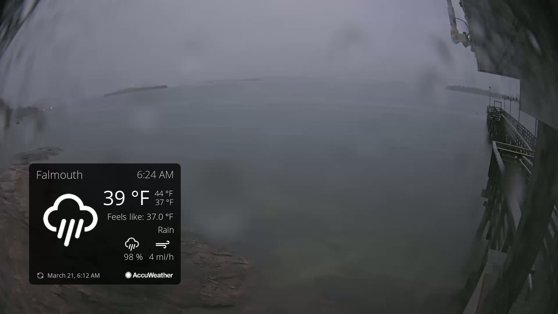 A rain-swept view from a pier shows a gray, overcast body of water under rainy conditions.