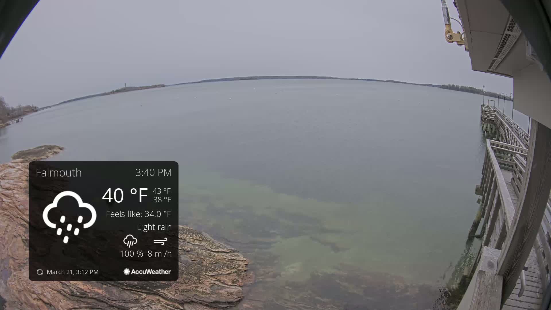 A calm body of water is seen from a wooden pier during light rain and overcast conditions.