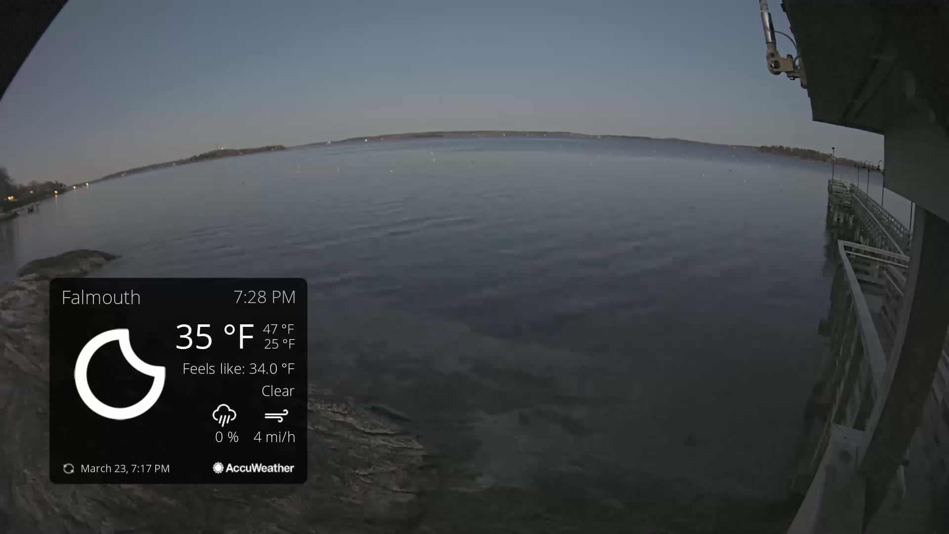 A calm body of water is seen at dusk from a pier under clear skies.