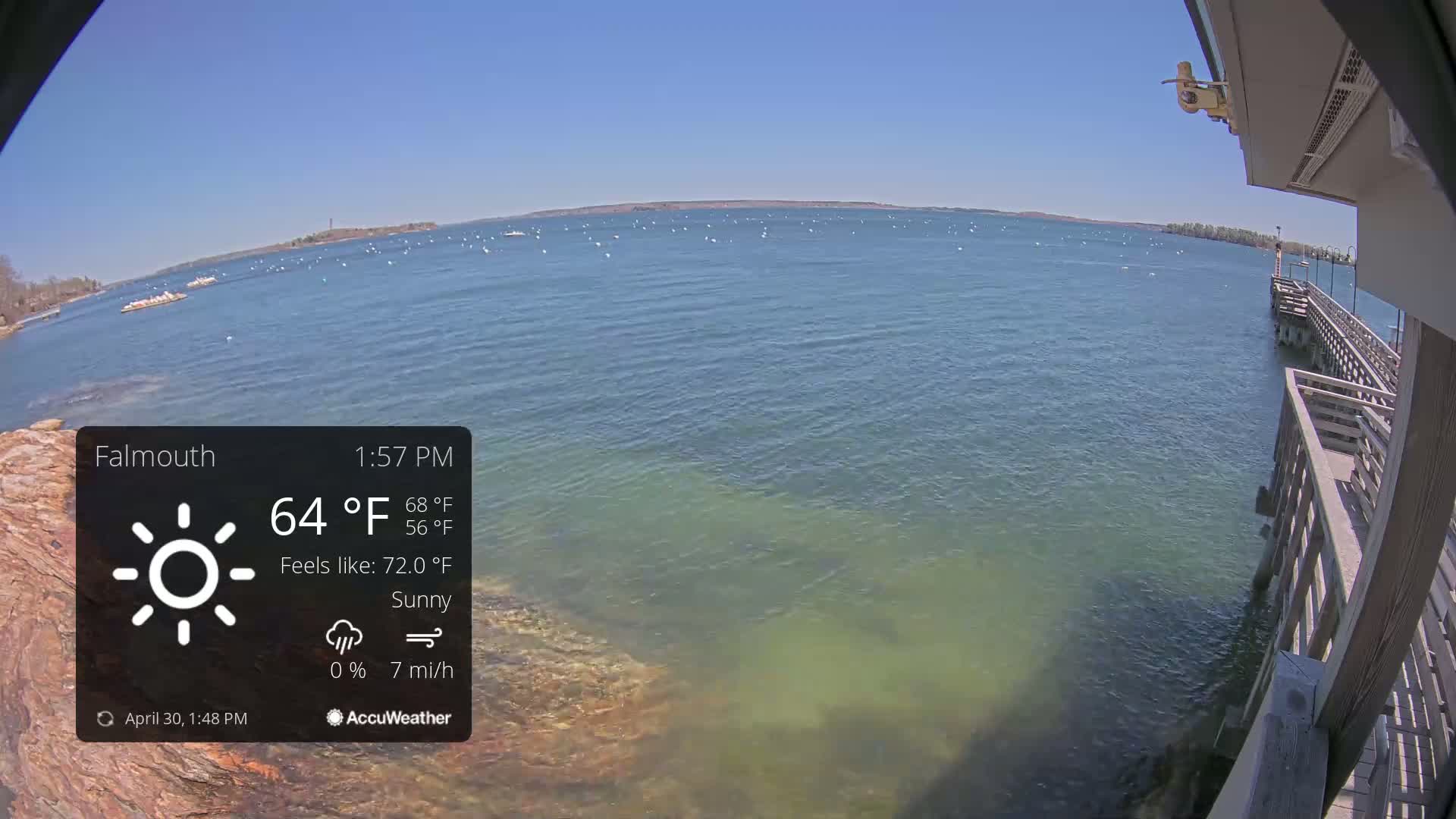 A sunny, calm day is shown with a view of a body of water, a distant shoreline, and a wooden pier extending from the right side of the image.