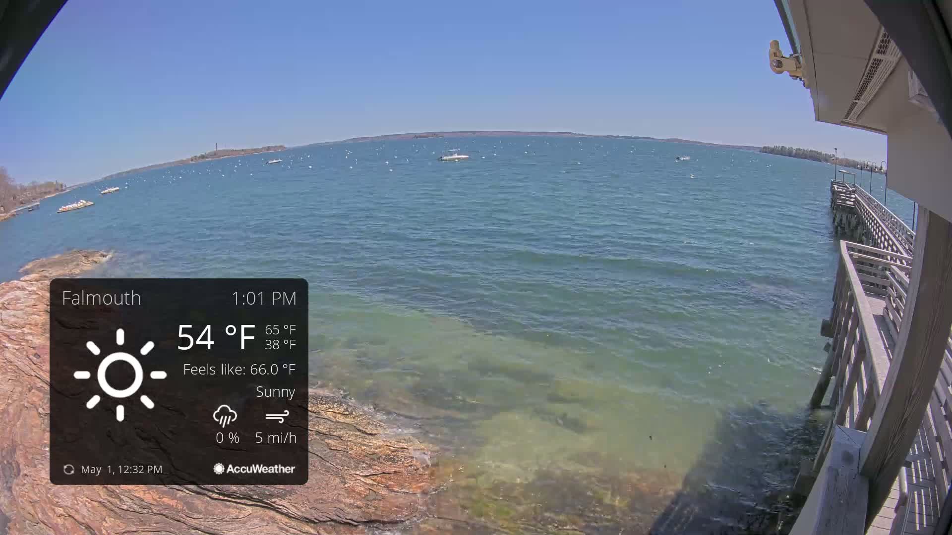 A sunny day on a body of water with several boats, seen from a pier with a rocky shoreline.