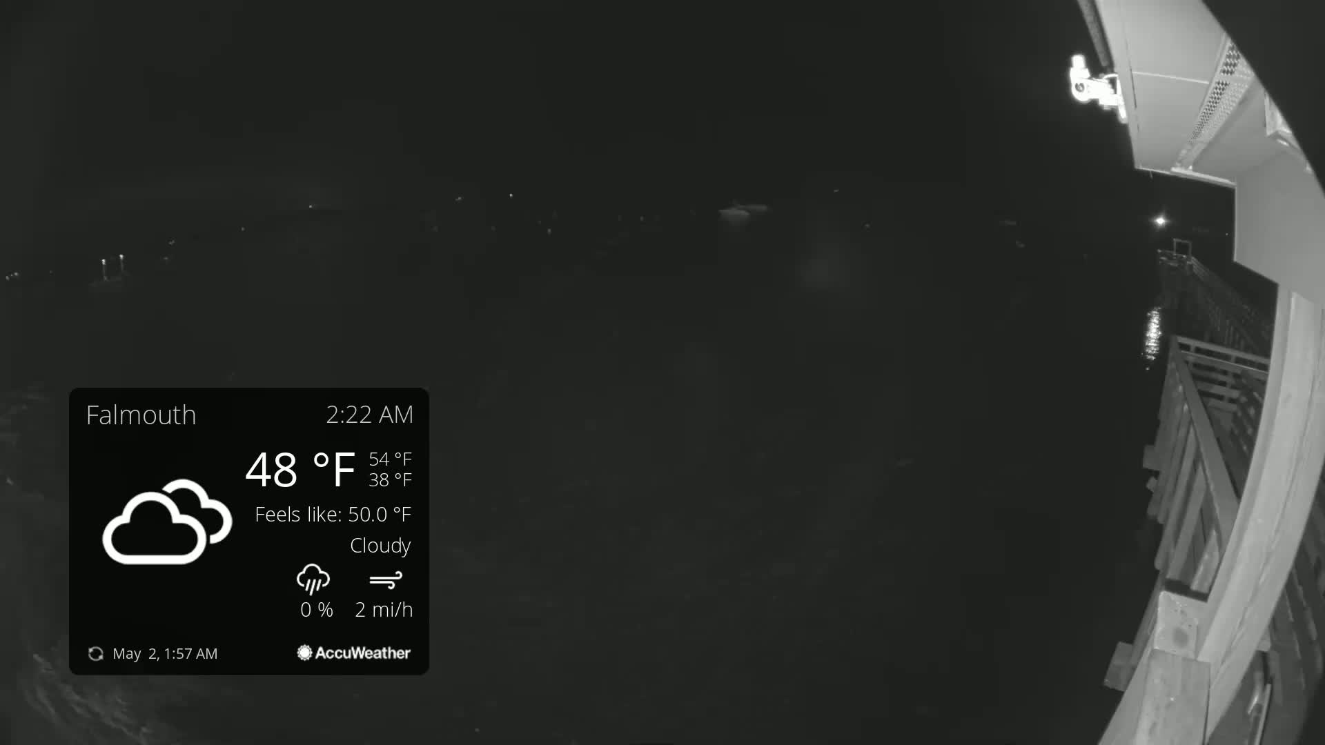 A nighttime, cloudy view from a security camera shows a dark body of water, a wooden deck, and a few distant lights.