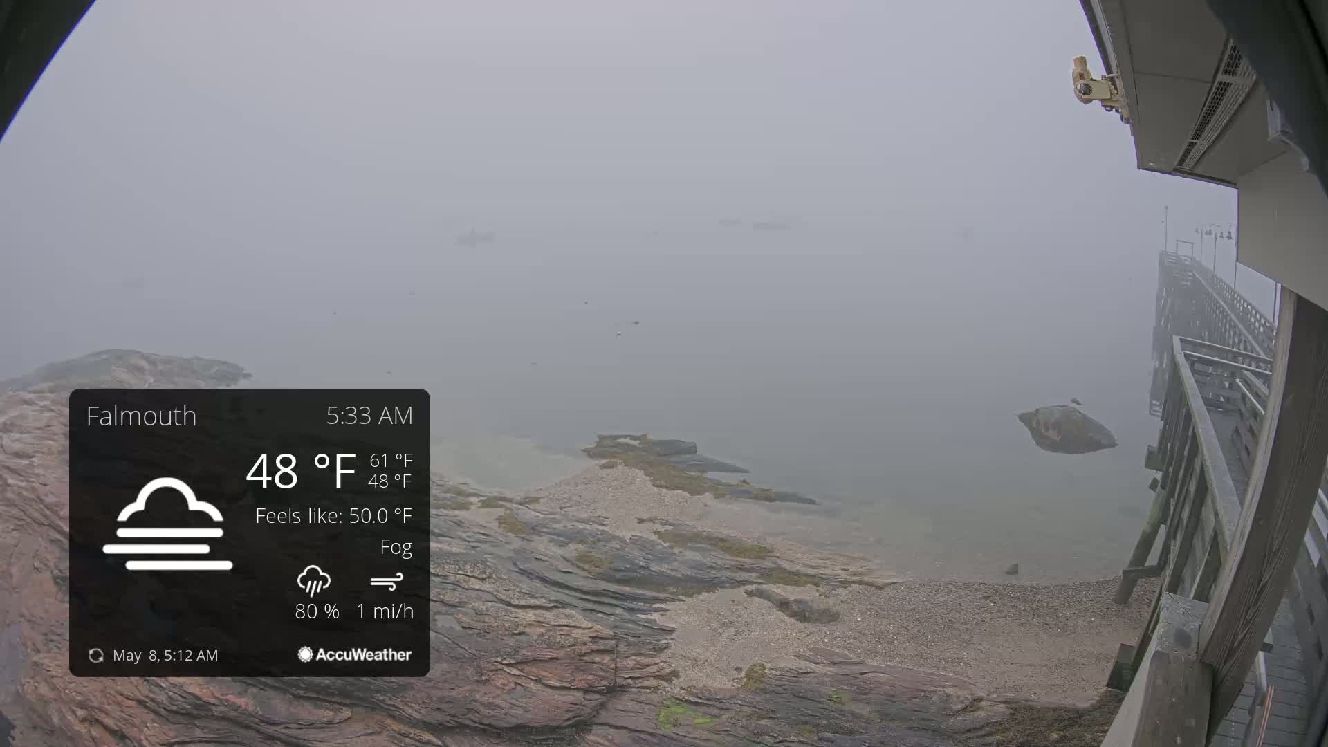 A foggy seaside scene shows a rocky shoreline and a wooden pier extending into the water.