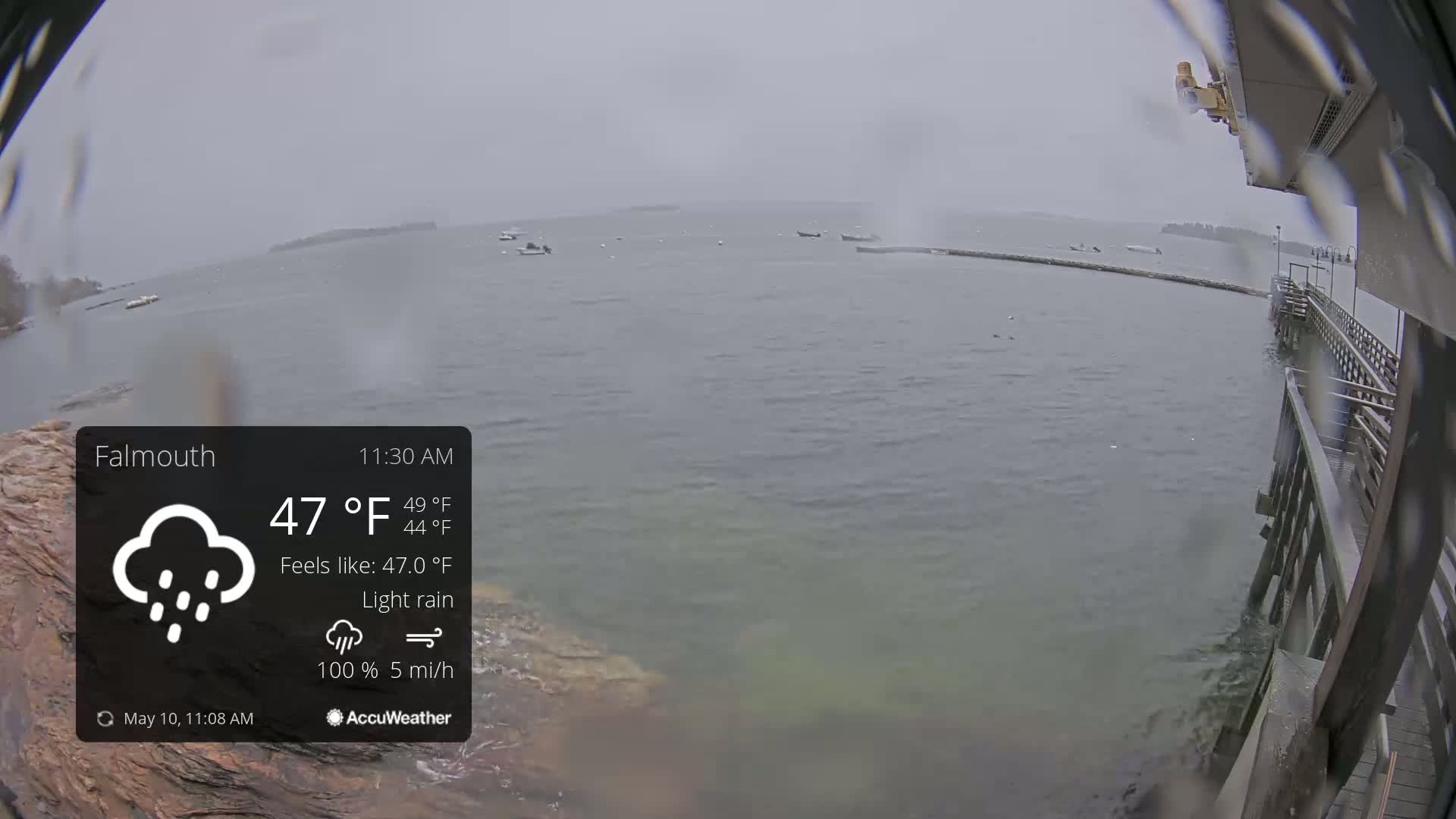 A view from a pier shows a calm body of water with several boats under a light rain.
