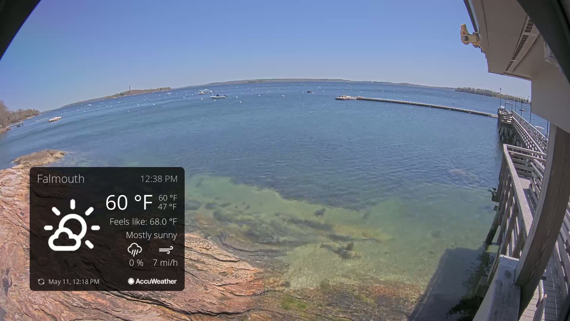 A mostly sunny, breezy day overlooking a calm body of water with several boats and a wooden pier.