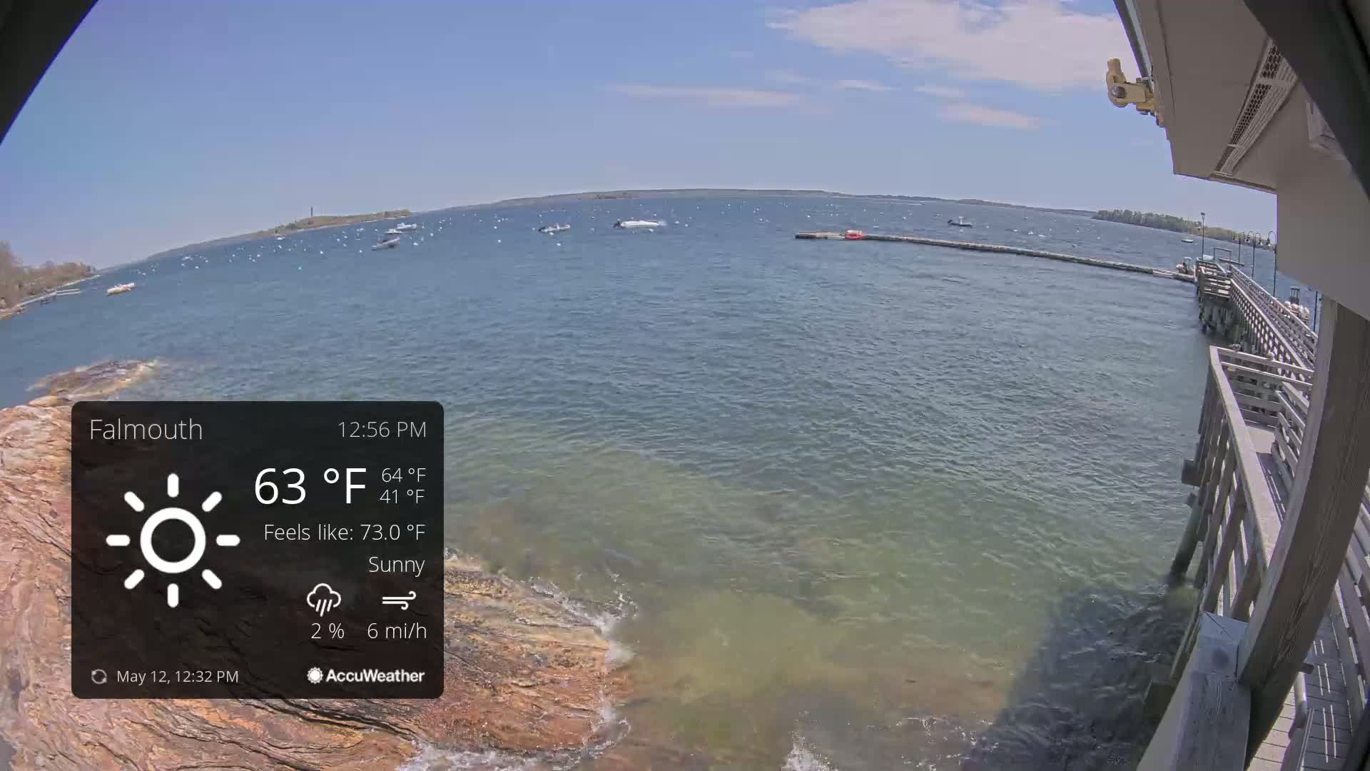 A sunny day overlooking a calm body of water with several boats, viewed from a wooden pier.
