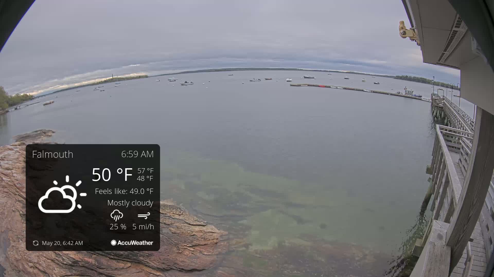 A mostly cloudy, 50°F morning view of a calm body of water with several boats, seen from a pier.