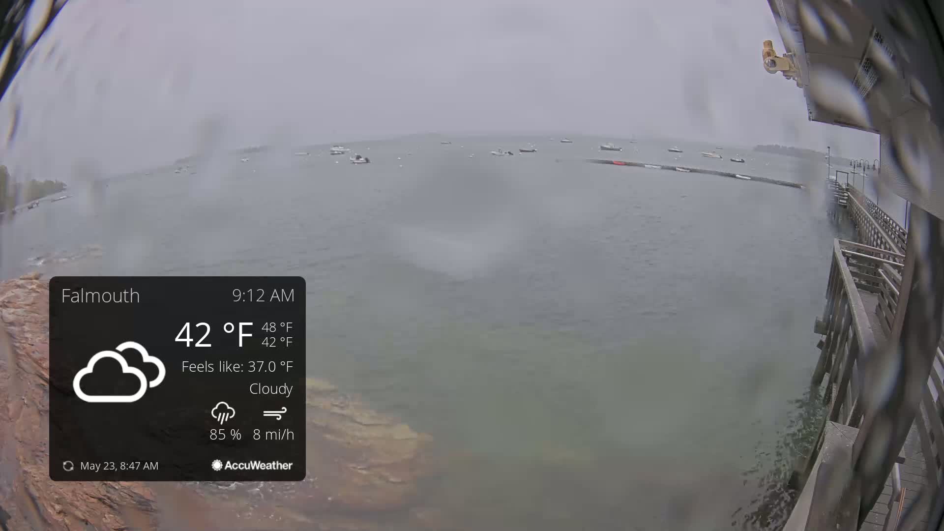 A cloudy, rainy day shows a body of water with several small boats, viewed from a wooden pier.