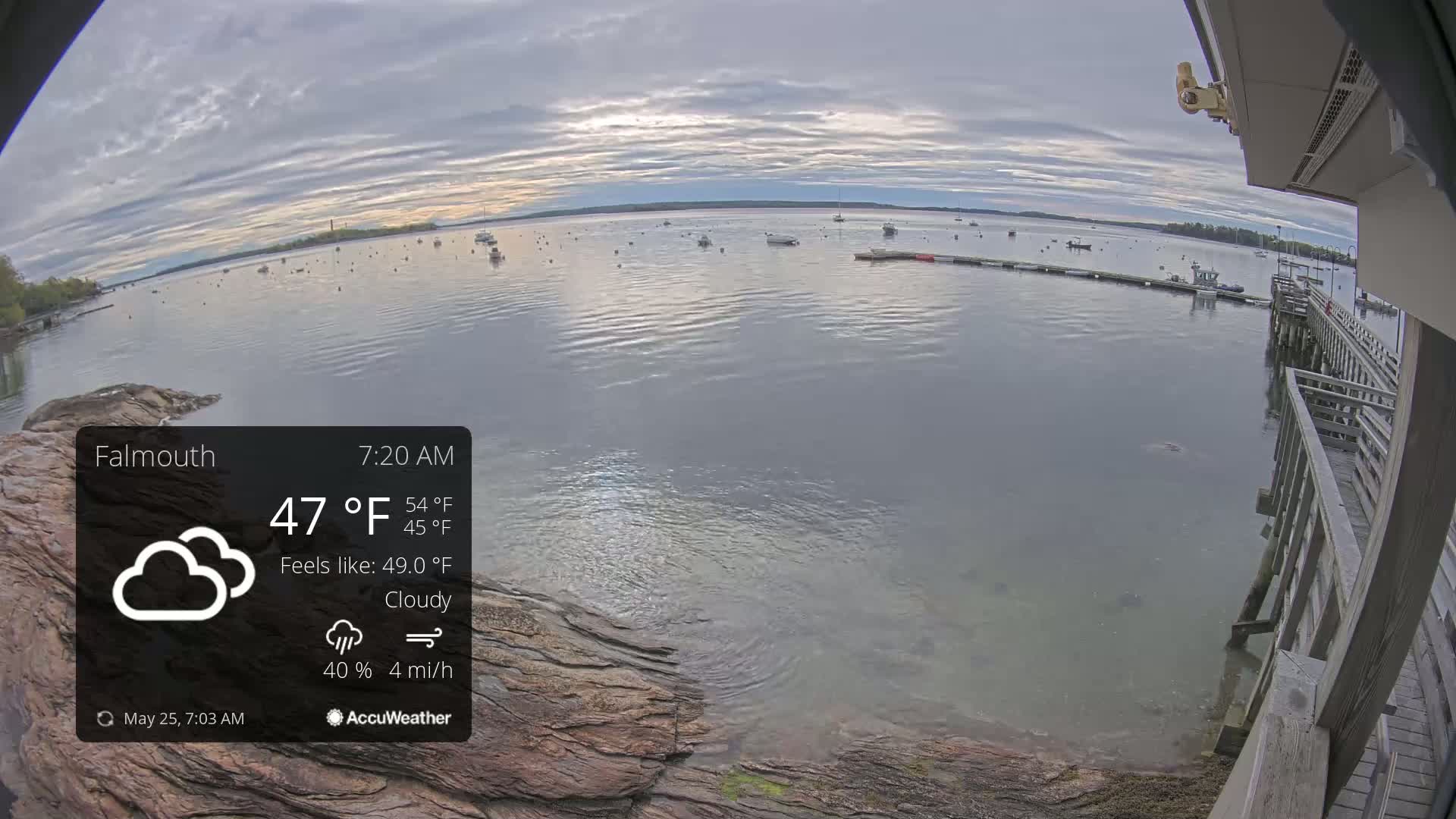 A cloudy morning view of a calm bay with numerous boats and a wooden pier, under a mostly cloudy sky.