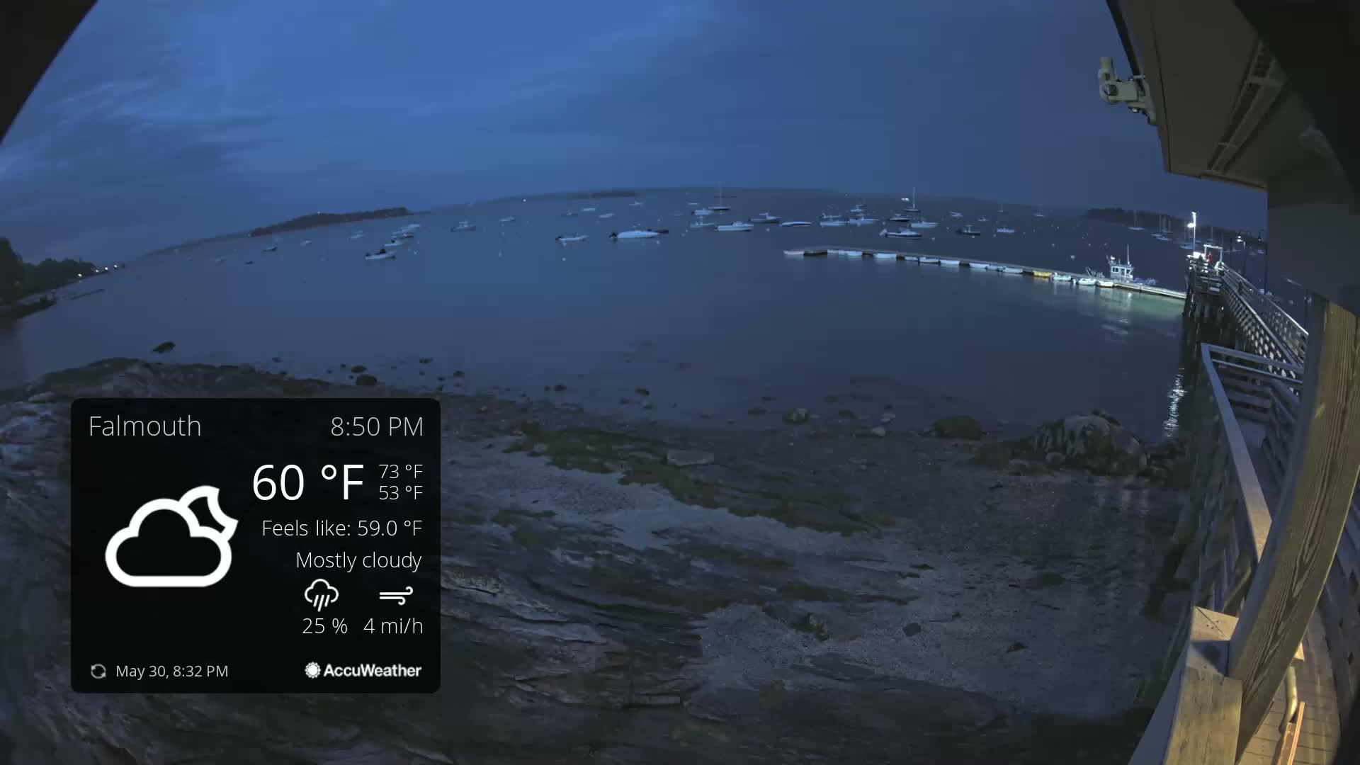 A mostly cloudy evening scene shows a body of water with numerous boats at a pier under a dark blue sky.