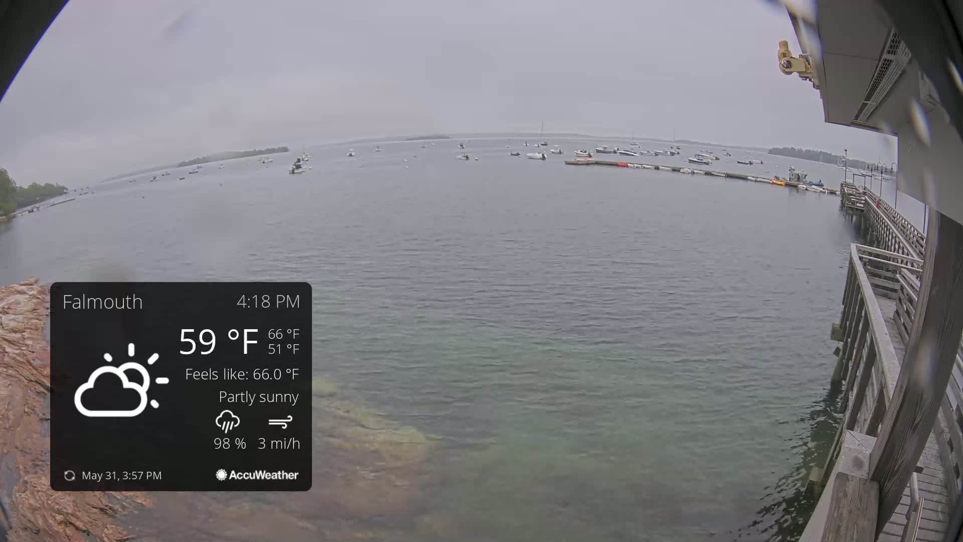 A partly sunny, overcast day with a light breeze shows numerous boats moored in a calm body of water next to a wooden pier.
