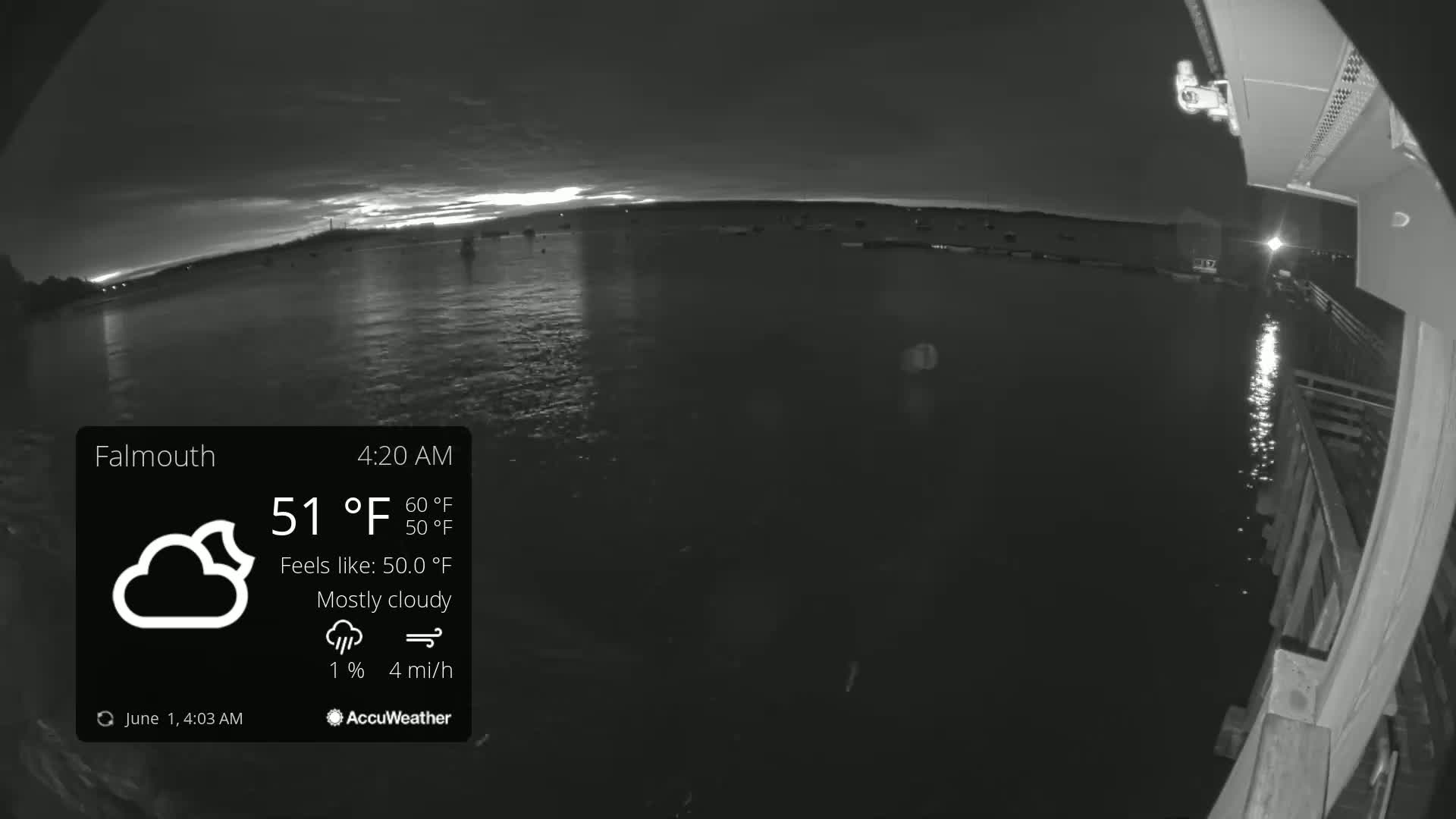 A mostly cloudy, pre-dawn view of calm water with boats visible in the distance, taken from a pier.