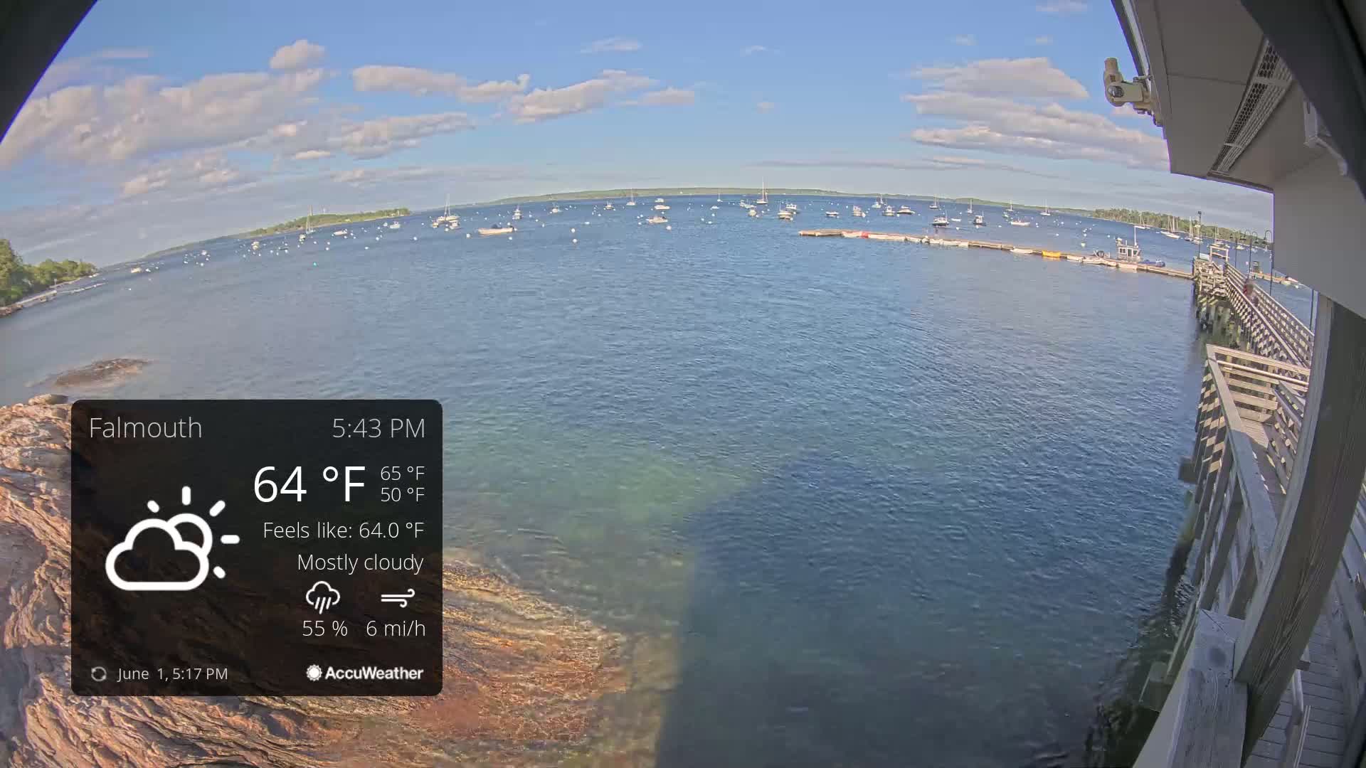 A mostly cloudy afternoon shows a calm body of water with numerous boats and a wooden pier extending from a building.