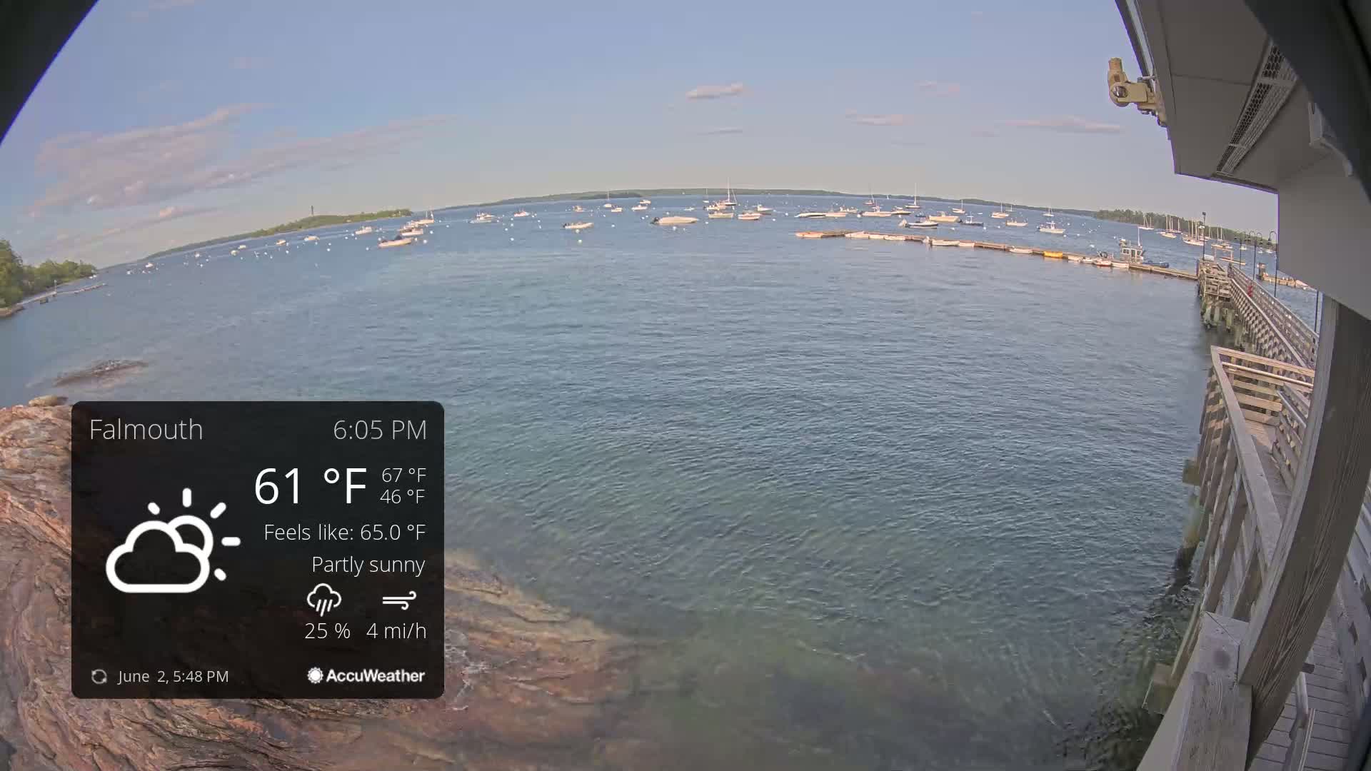 A partly sunny view of a calm body of water with numerous boats, seen from a wooden pier on a partly sunny day.
