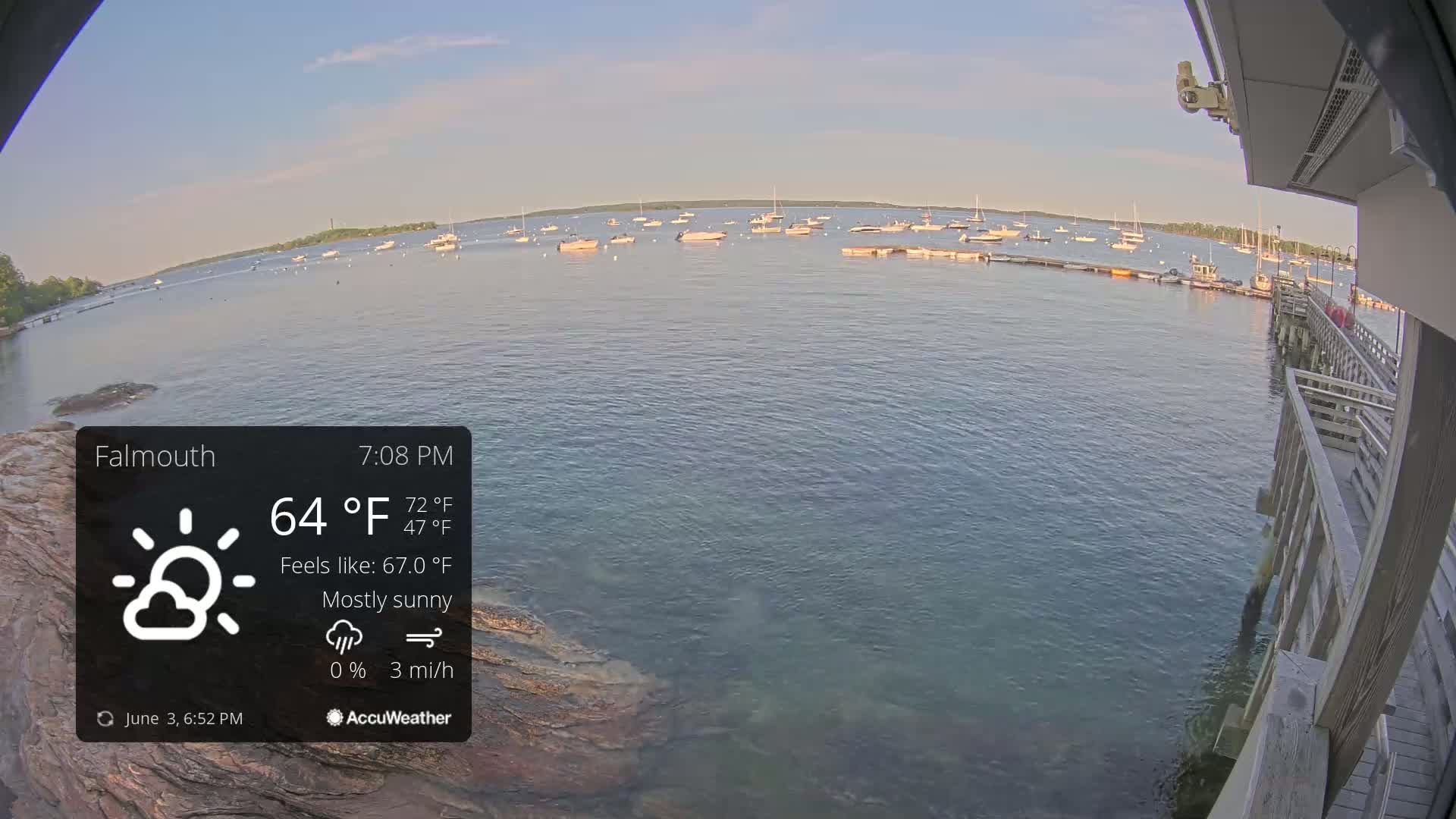 A mostly sunny, calm evening scene shows numerous boats in a harbor from a waterfront pier.