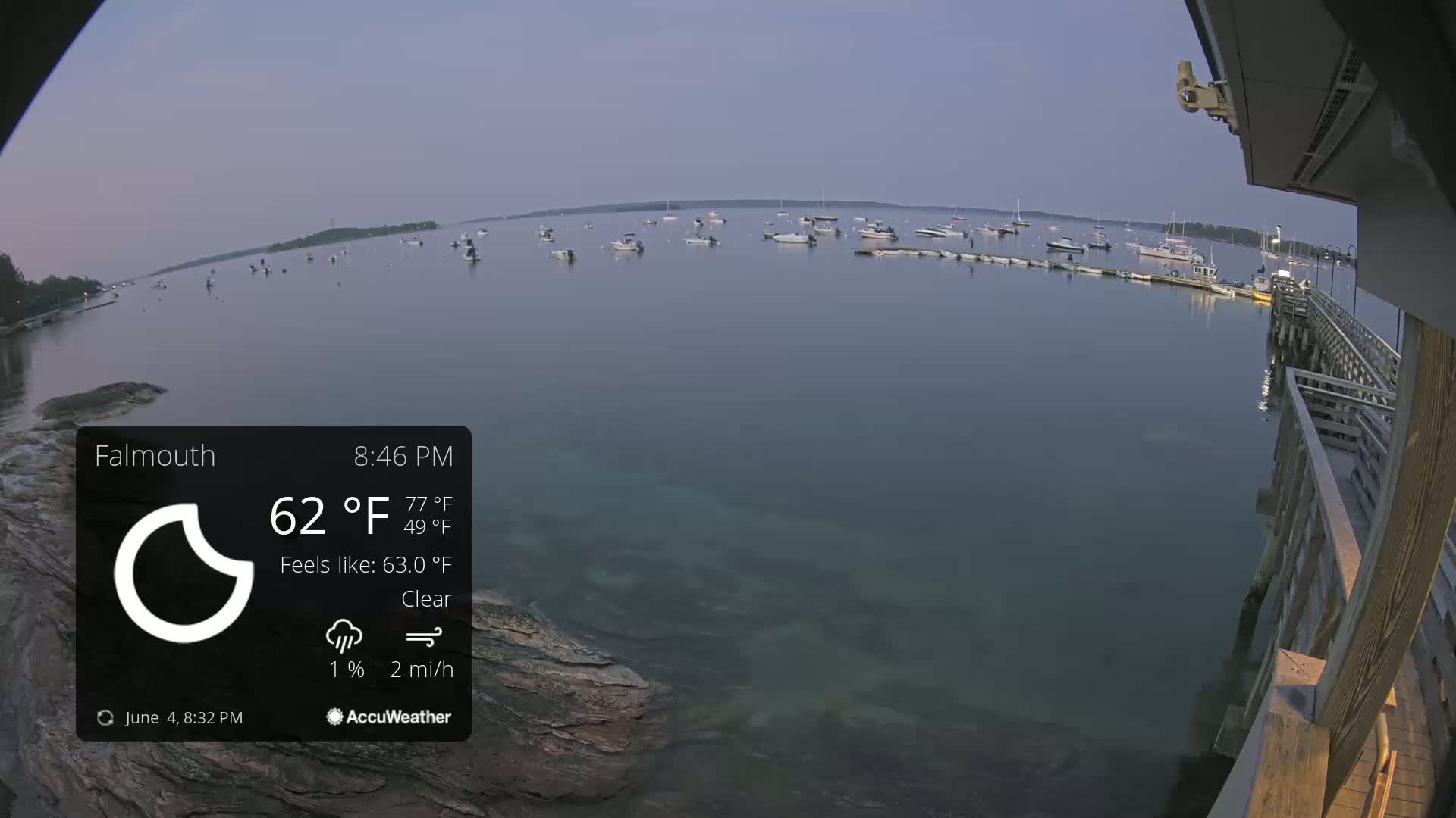 Numerous boats are moored in a calm, clear body of water at dusk, viewed from a wooden pier.