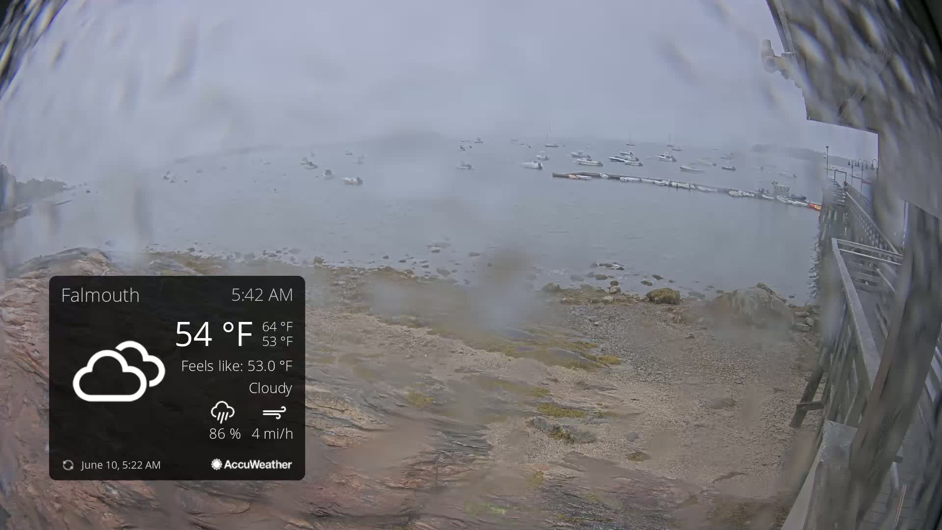 A cloudy, rainy morning shows a rocky shoreline with several boats in the water.