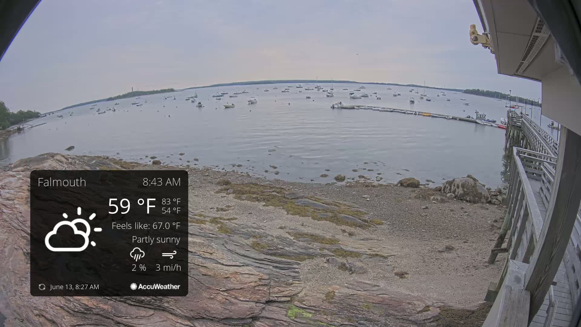 A partly sunny view of a rocky shoreline with numerous boats on the water under a gray sky.