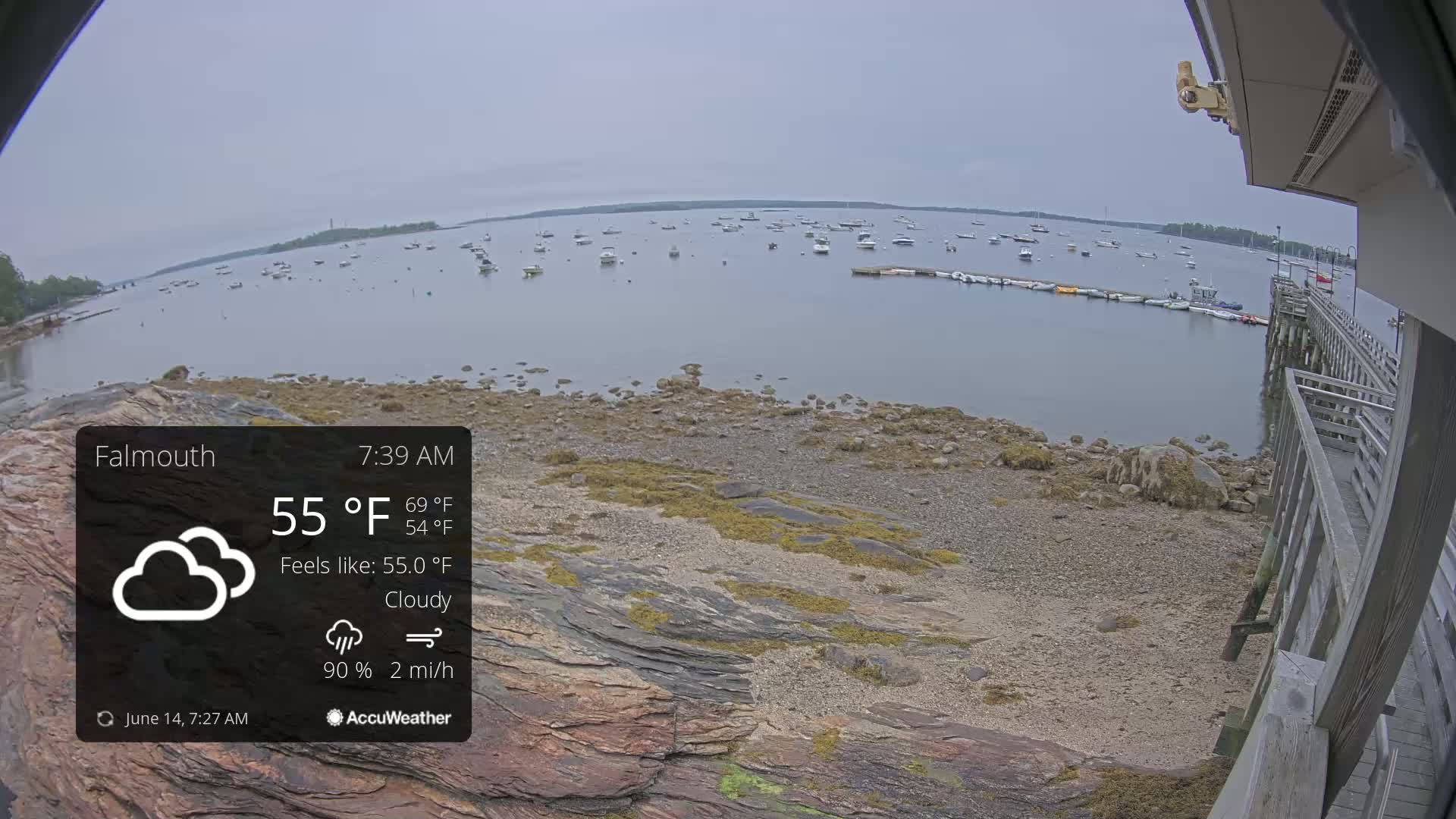 A cloudy, 55°F morning shows a rocky shoreline with numerous boats in a calm bay, viewed from a wooden pier.