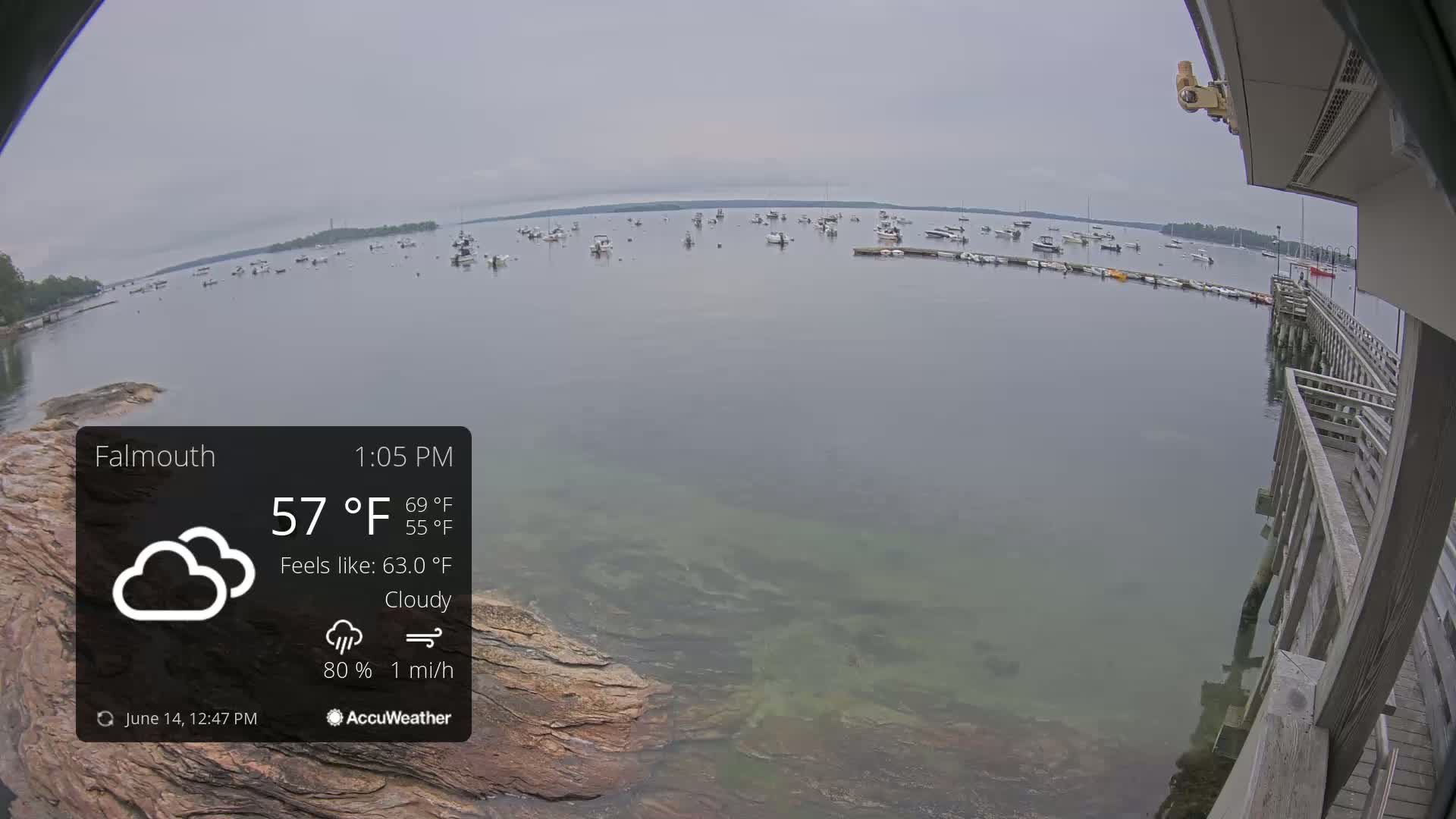A cloudy, calm day on a body of water with numerous boats moored, viewed from a wooden pier.