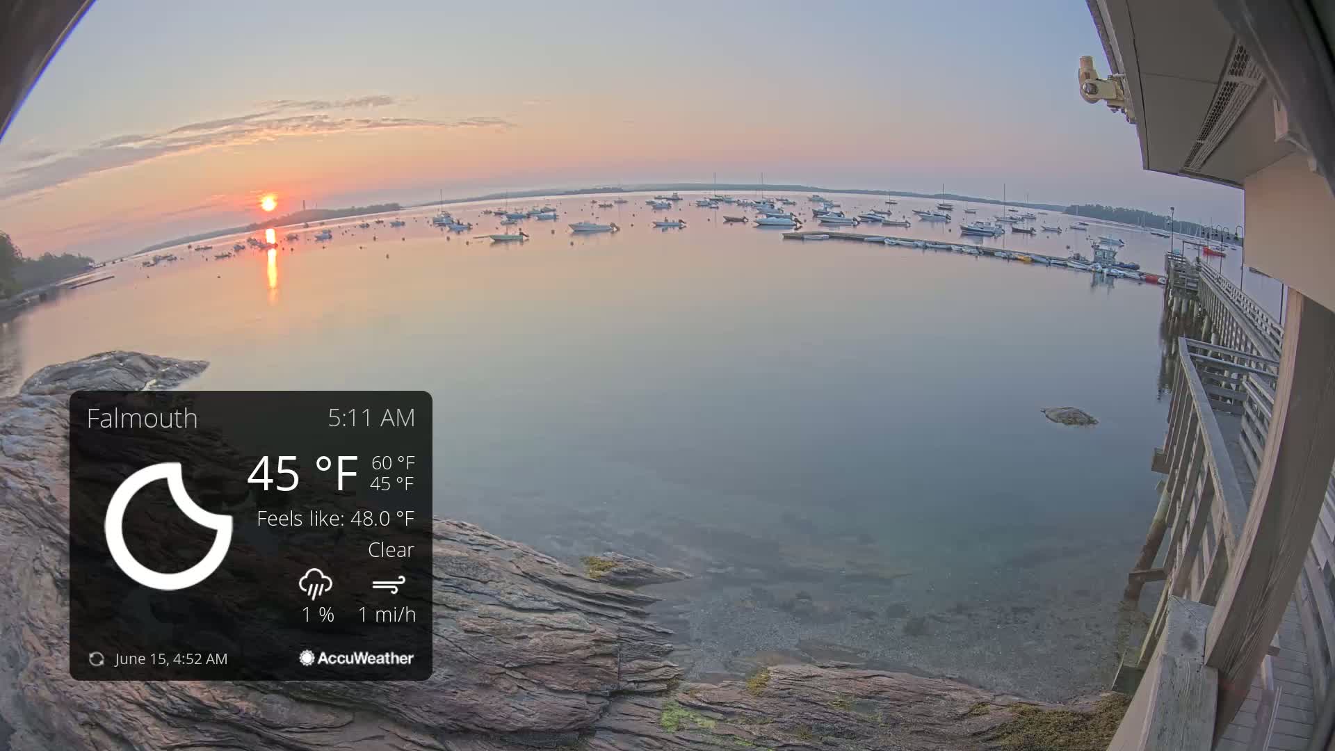 A calm body of water with numerous boats at sunrise, viewed from a wooden dock under clear skies.