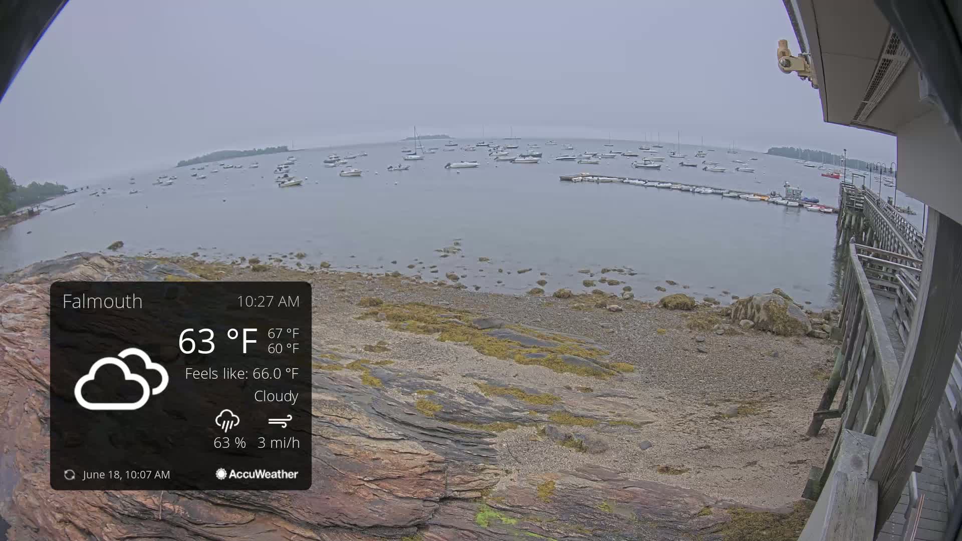 A cloudy, overcast day shows a rocky shoreline with many boats in a calm bay.