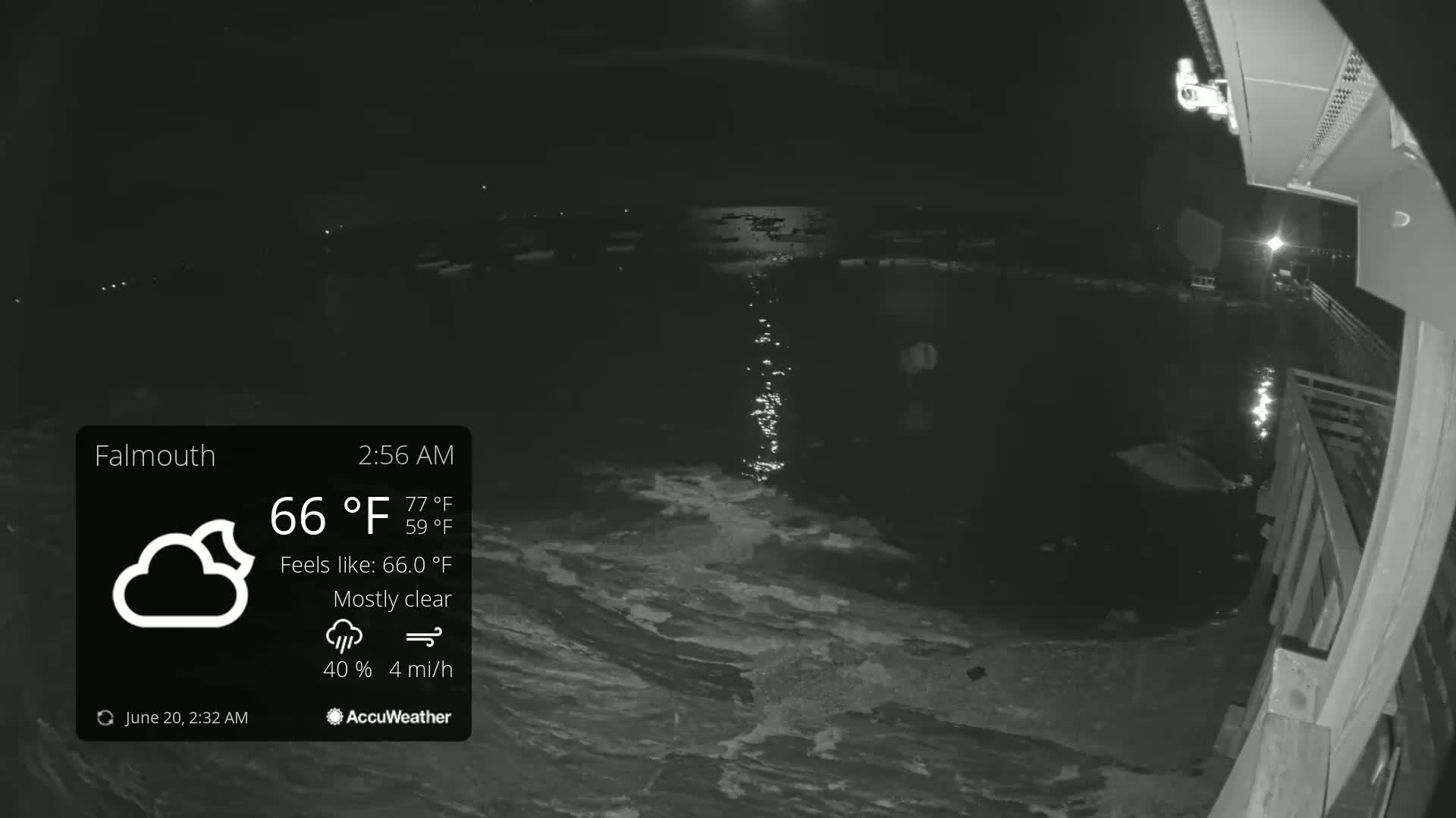 A nighttime, mostly clear view of a body of water from a waterfront deck, with a light breeze.