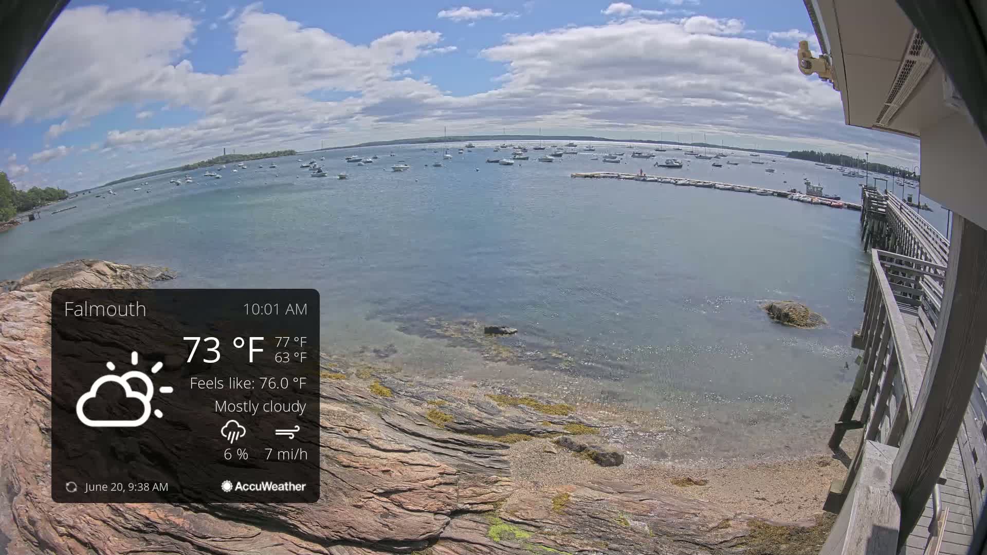 A mostly cloudy, 73°F day shows a calm body of water with numerous boats and a rocky shore with a wooden pier.