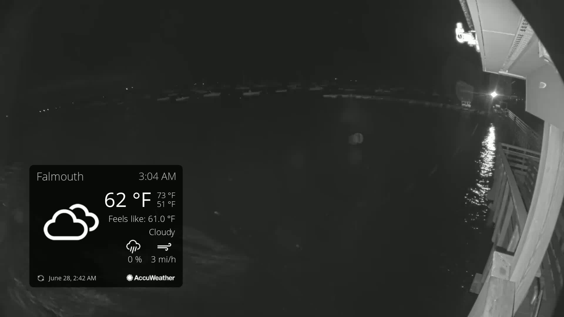 A nighttime, cloudy view of a calm body of water with a dimly lit shoreline, under a 62°F temperature.