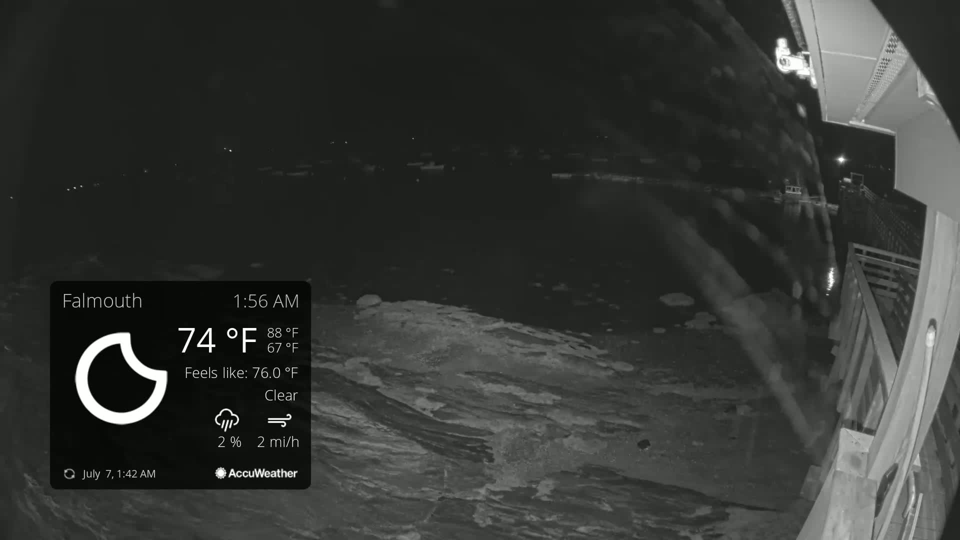 A nighttime, clear view of dark water shows a rocky shoreline next to a wooden deck under a clear sky.
