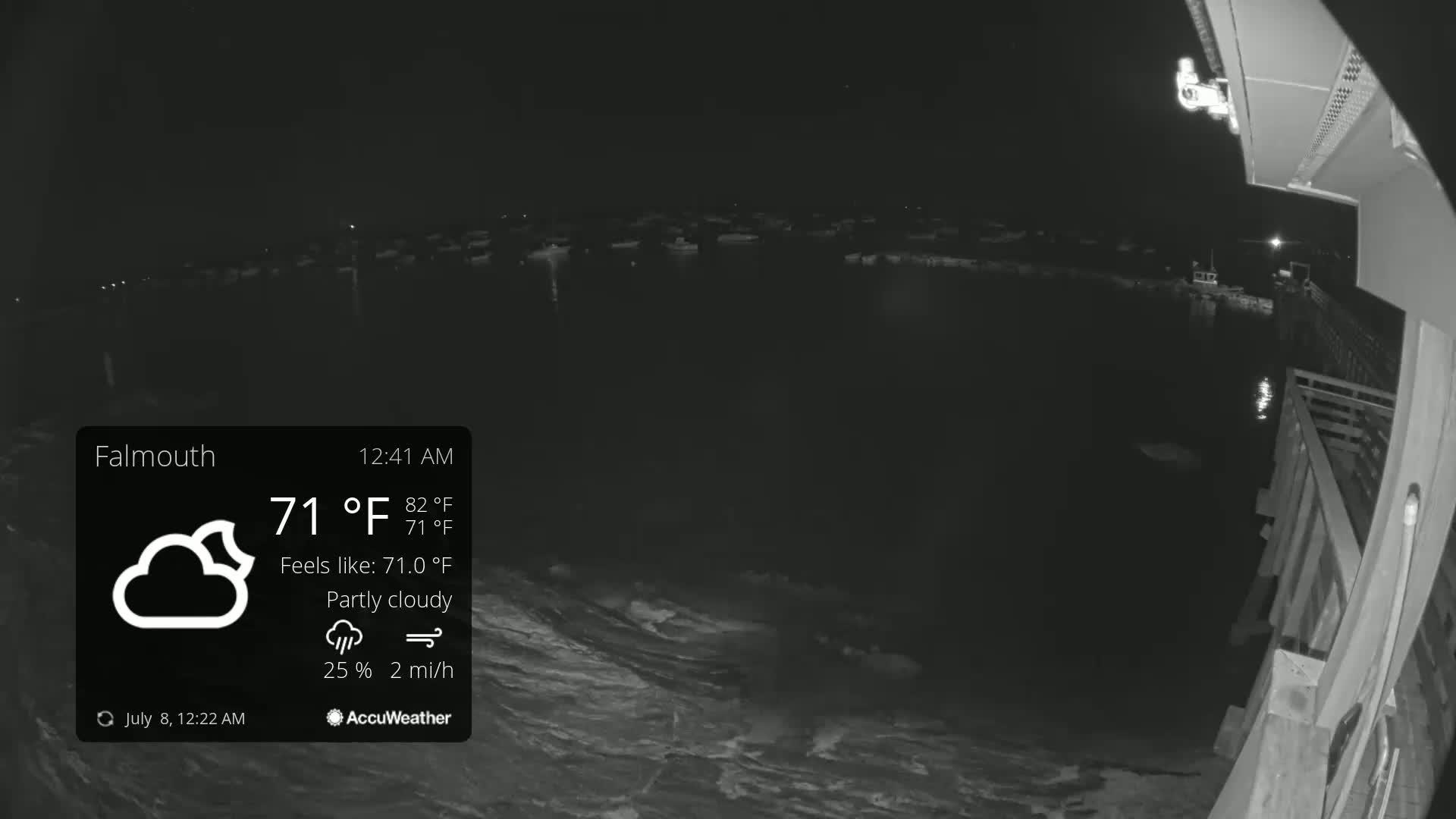 A nighttime, partly cloudy scene shows a body of water with numerous boats moored, viewed from a wooden structure under a 71°F temperature.