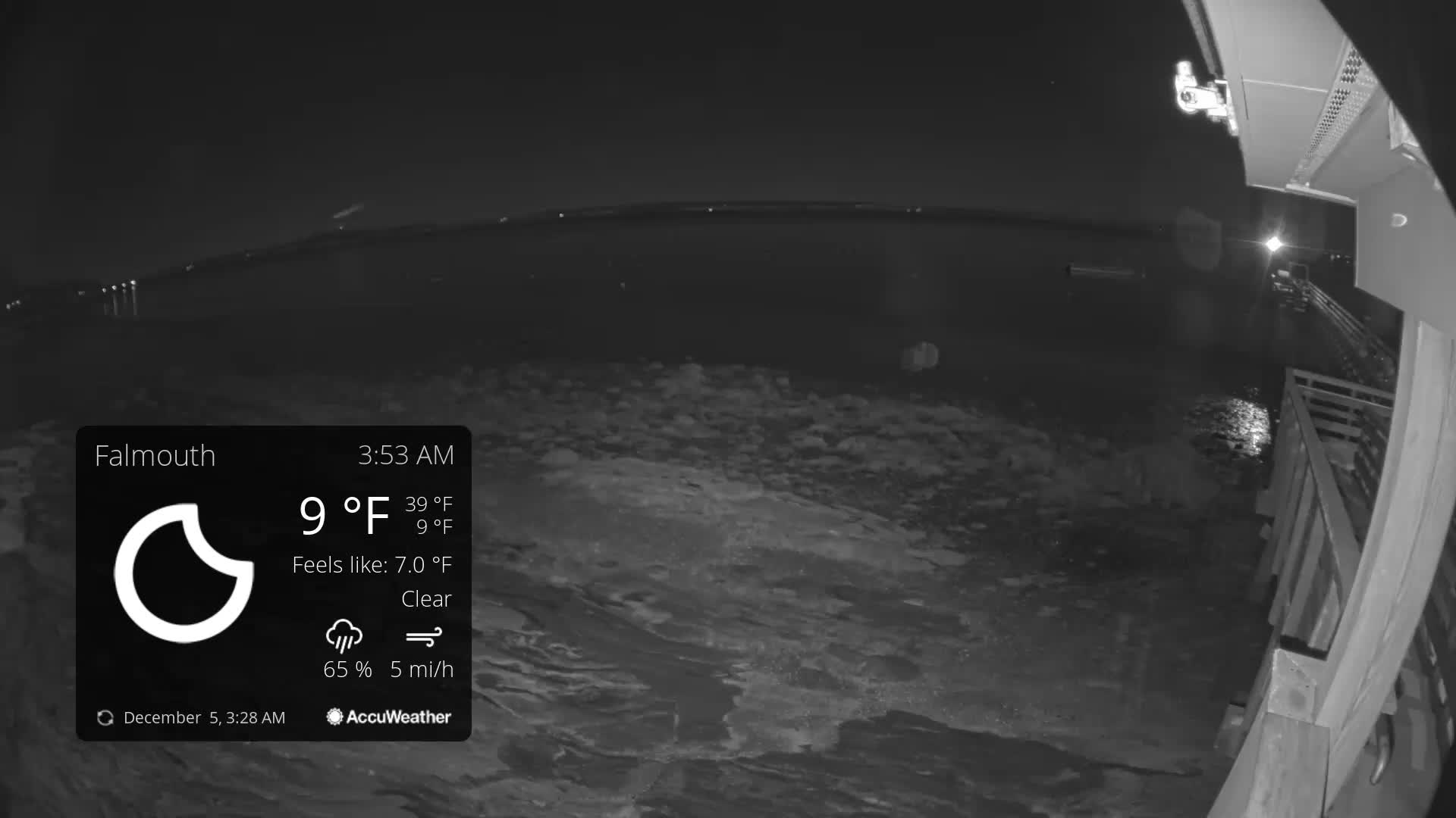 The image displays a dark, outdoor night scene of a body of water partially covered in ice or slush, with distant lights on a shoreline and a wooden structure visible on the right, under clear and cold conditions.