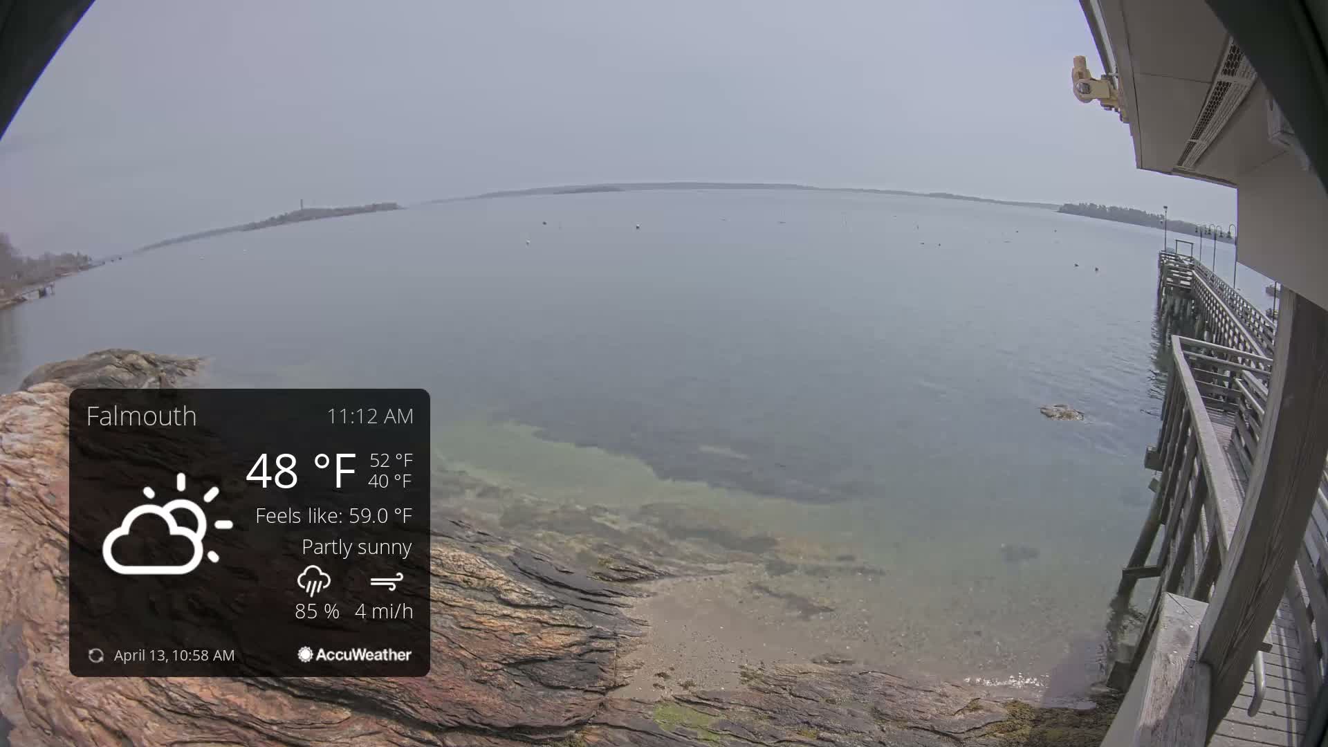 The image displays a dark, outdoor night scene of a body of water partially covered in ice or slush, with distant lights on a shoreline and a wooden structure visible on the right, under clear and cold conditions.