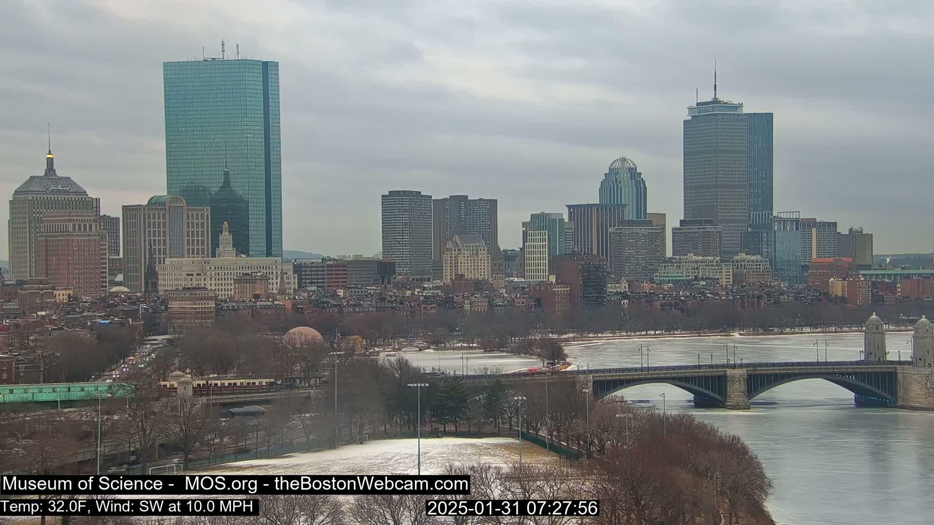 A city skyline with numerous skyscrapers and buildings is visible across a partly frozen river under an overcast sky.
