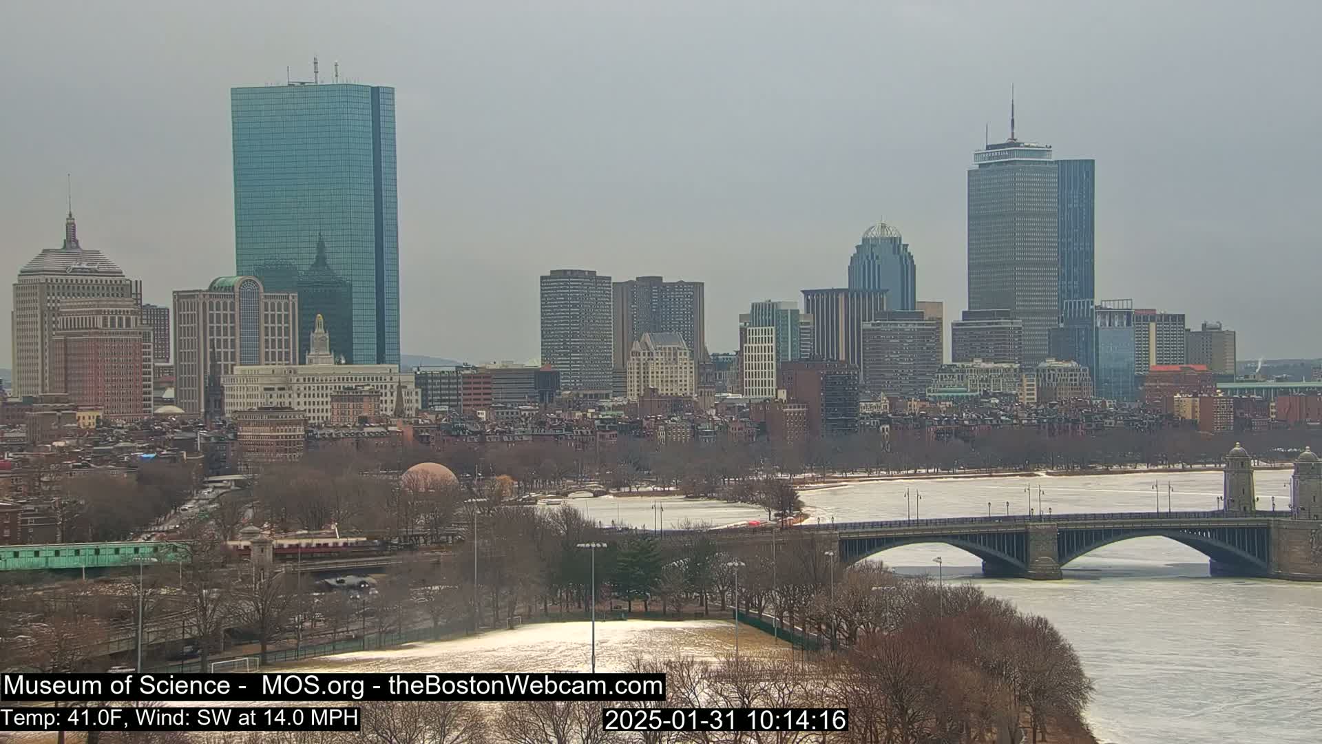 A cityscape with numerous skyscrapers is visible across a partially frozen river, under an overcast sky.