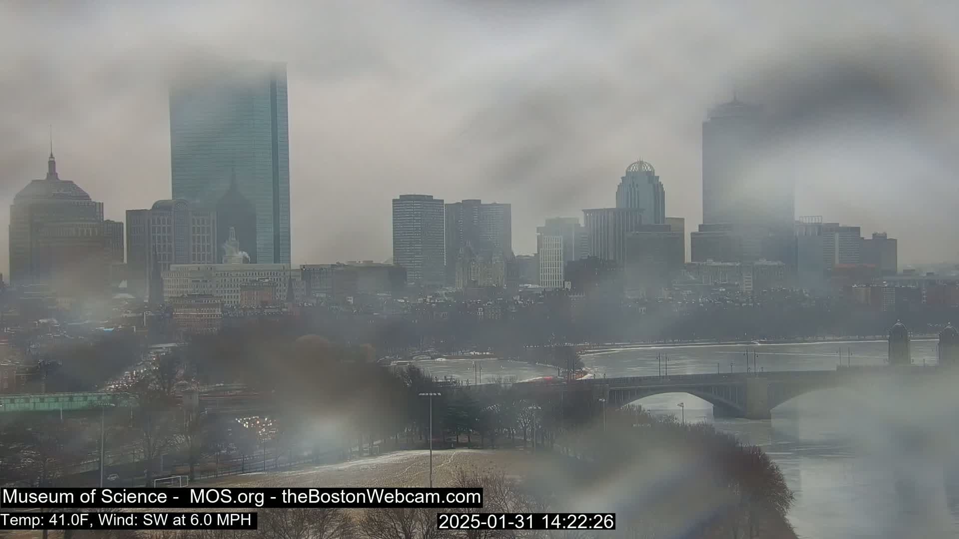 A foggy view of a city skyline, featuring numerous skyscrapers and a bridge over a river, with the temperature at 41°F and a southwest wind of 6.0 mph.