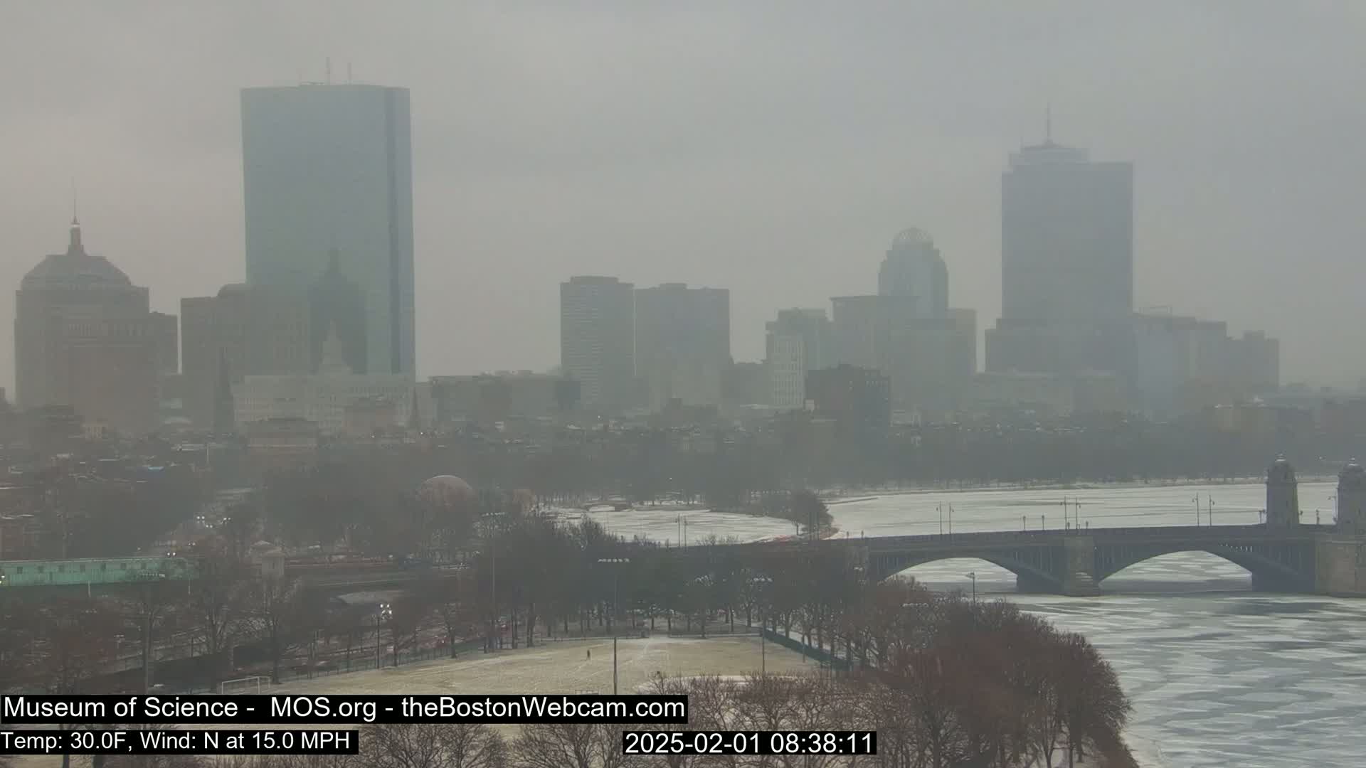 A hazy, snowy cityscape with a bridge over a partially frozen river is visible on a 30°F day with a 15 mph north wind.