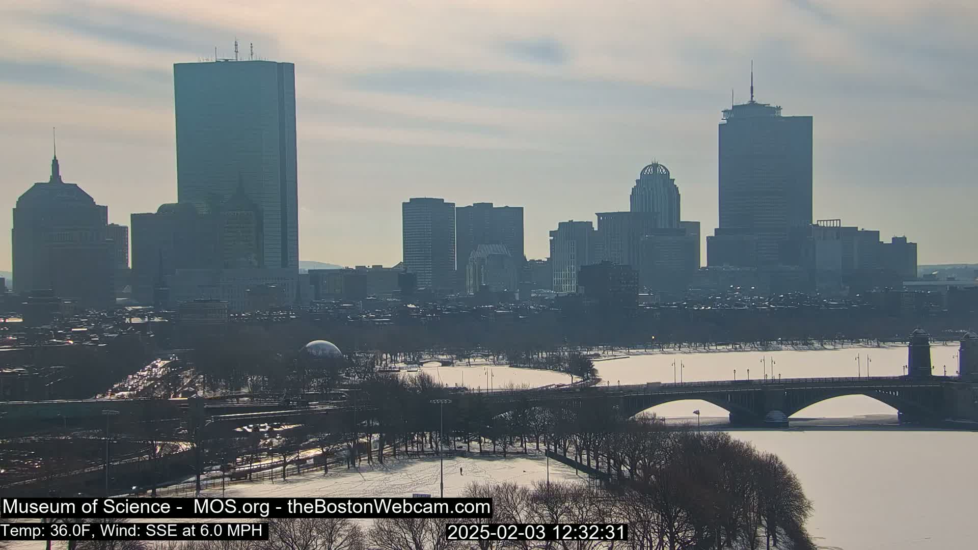A snow-covered cityscape with a river and bridge is visible under a hazy sky.