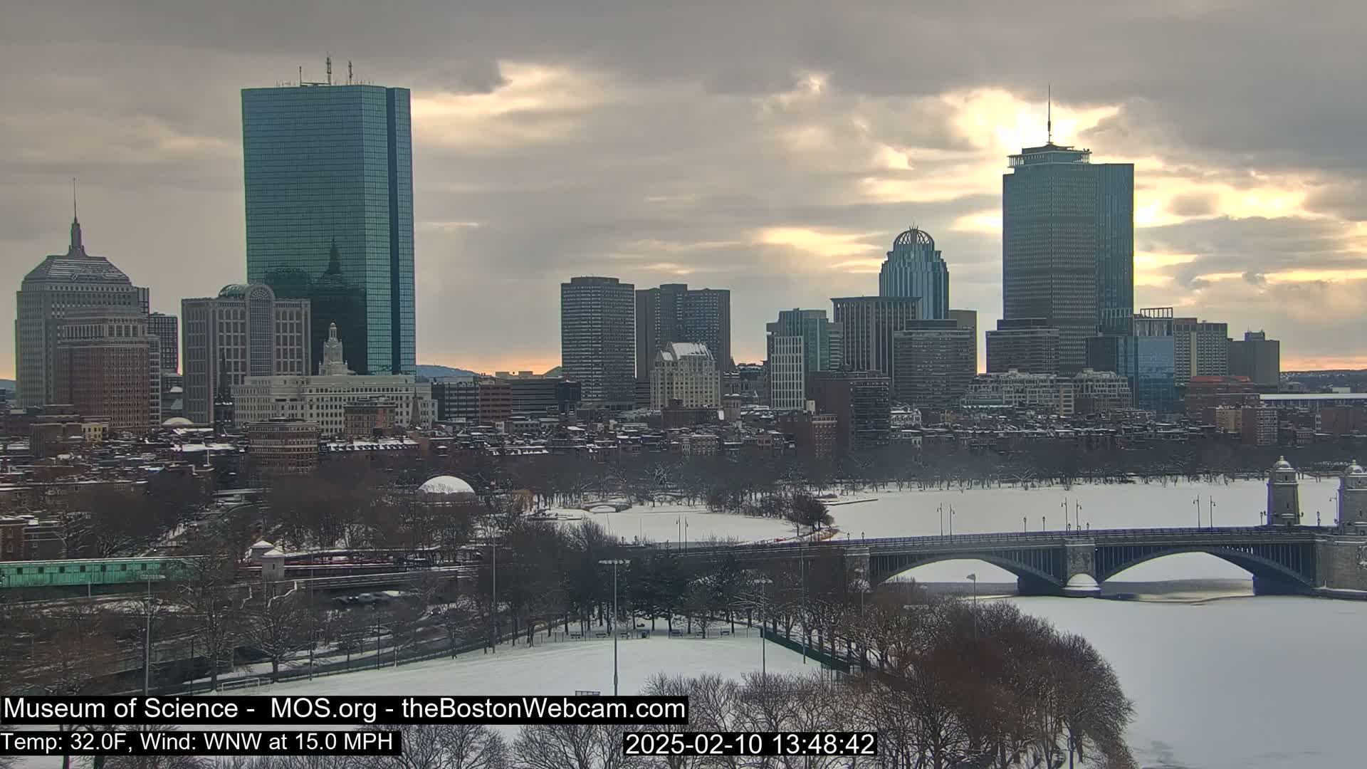 A snow-covered city skyline, including several skyscrapers and a bridge over a frozen river, is visible under a partly cloudy sky.