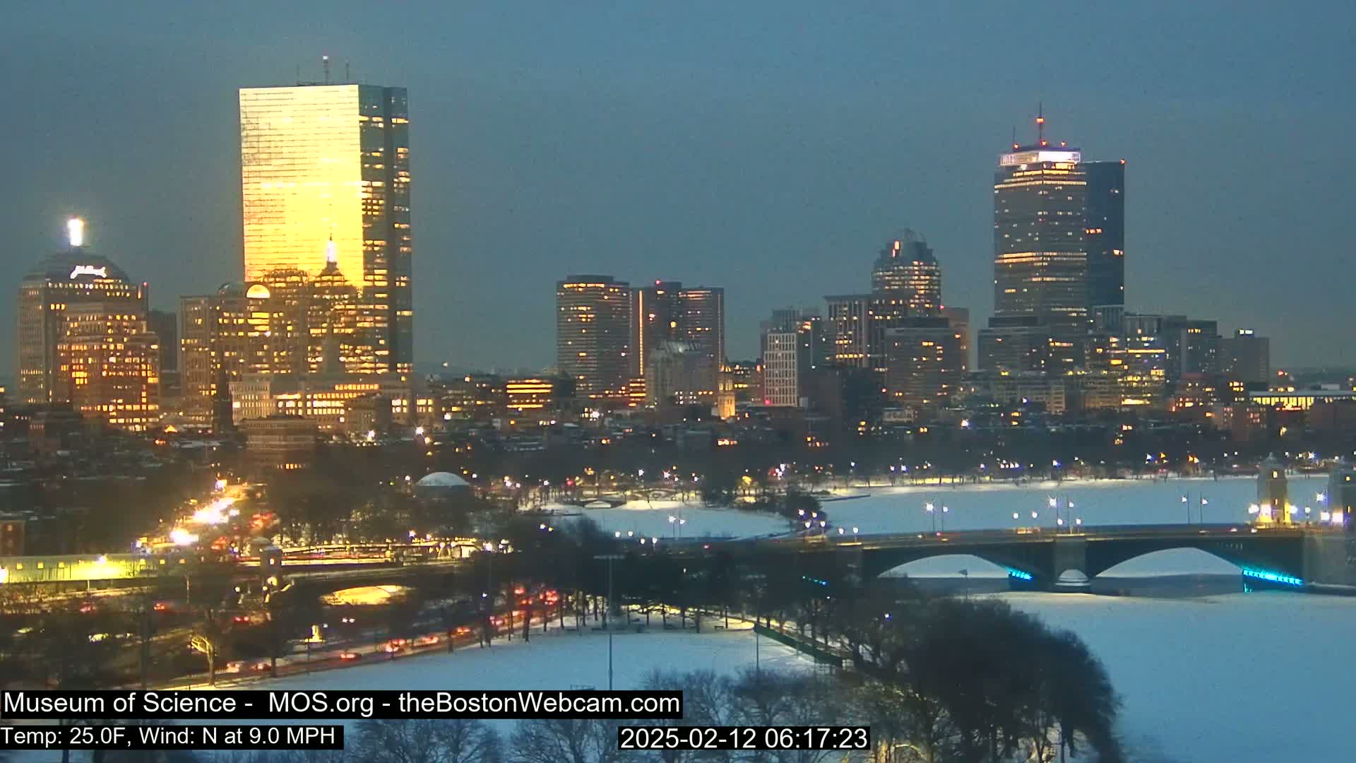 A nighttime cityscape with illuminated skyscrapers and bridges, partially covered in snow, under a twilight sky.