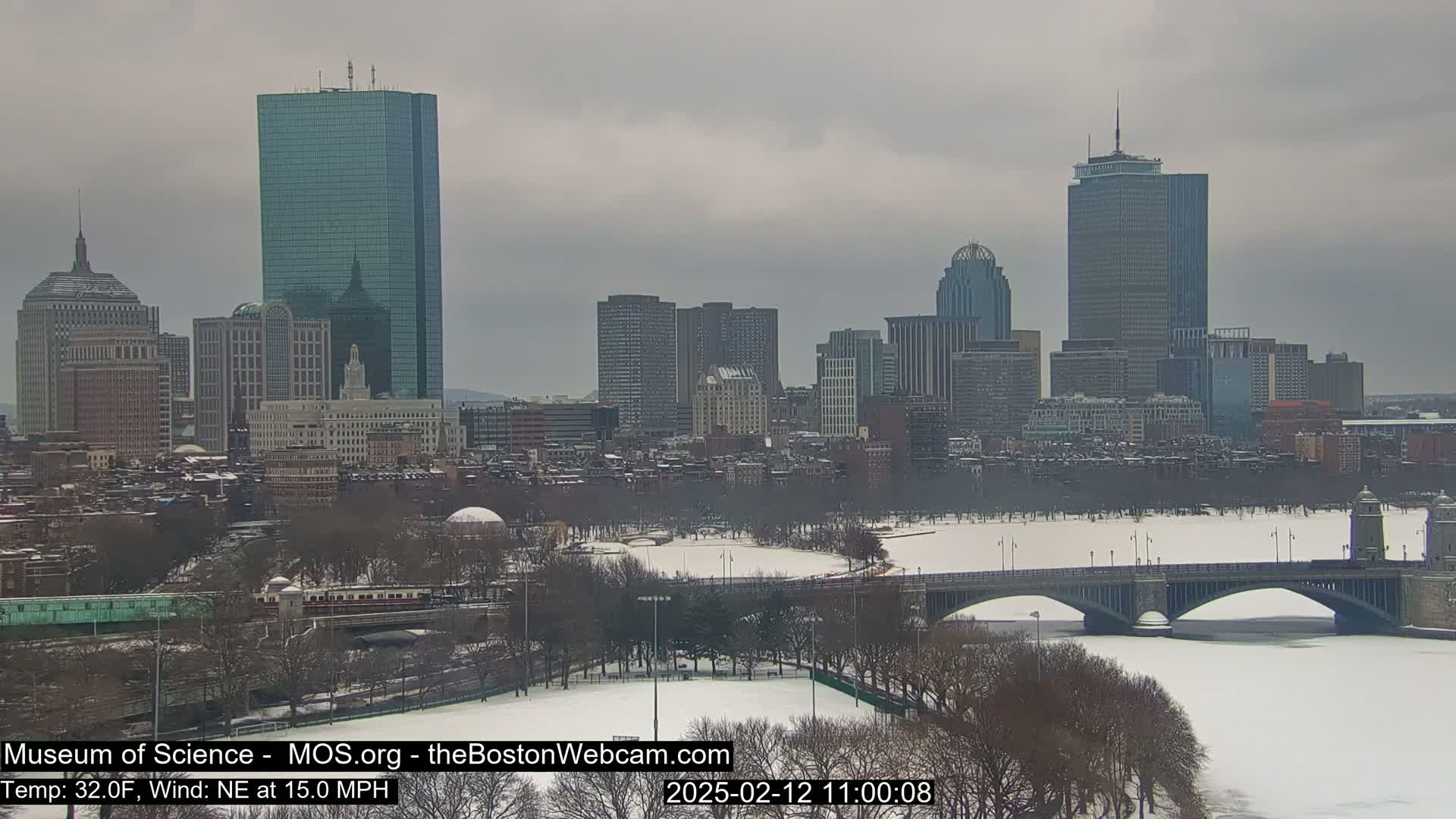 A snow-covered cityscape, including a bridge over a frozen river, is visible under an overcast sky.