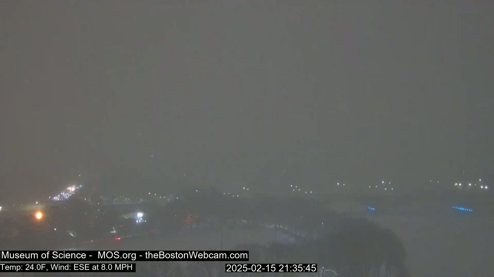A hazy, nighttime view of a landscape under snowy conditions with faint lights visible in the distance.