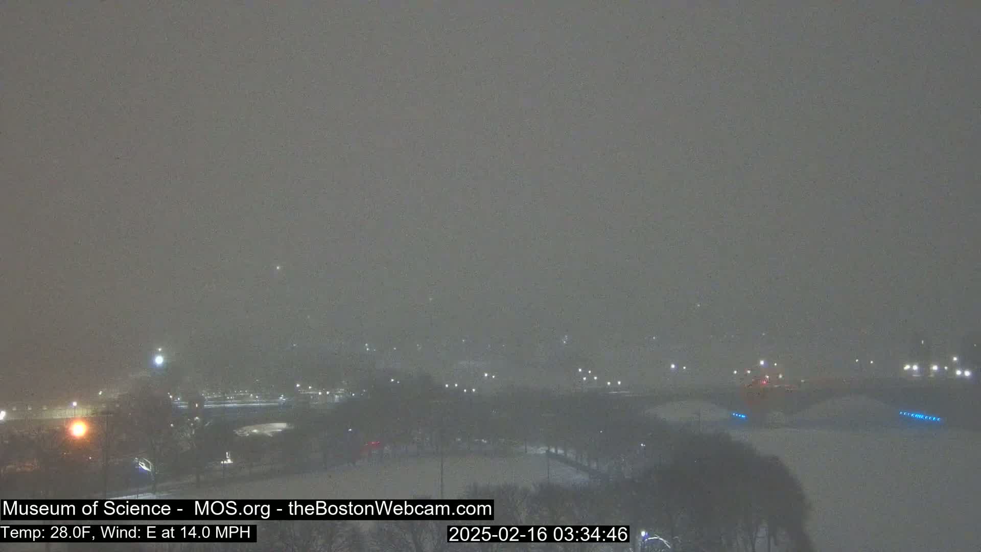 A snow-covered landscape at night is visible under heavy snowfall with a strong easterly wind.