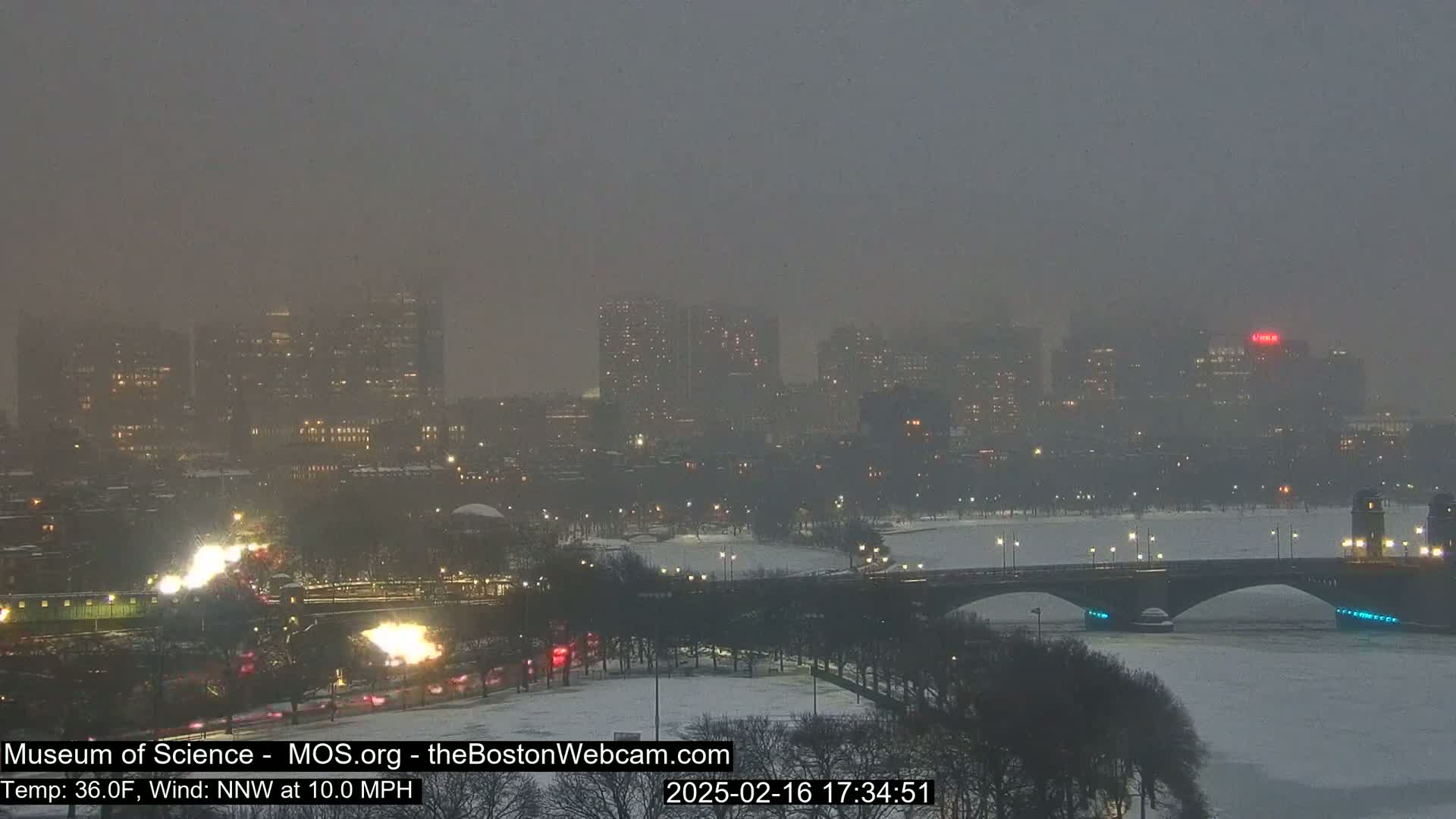 A snow-covered city skyline with a bridge over a partially frozen river is visible under a hazy, dark sky.