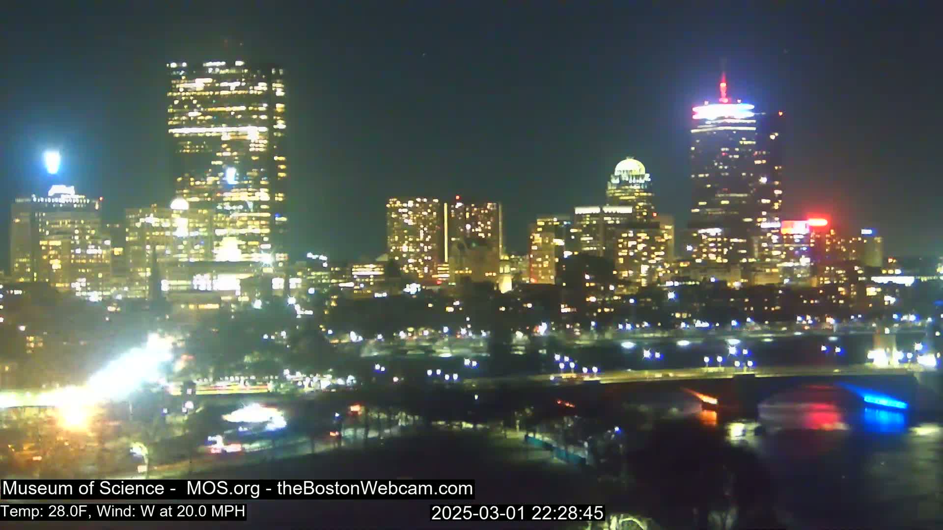 A brightly lit city skyline at night, with a 20 mph west wind and a temperature of 28 degrees Fahrenheit.