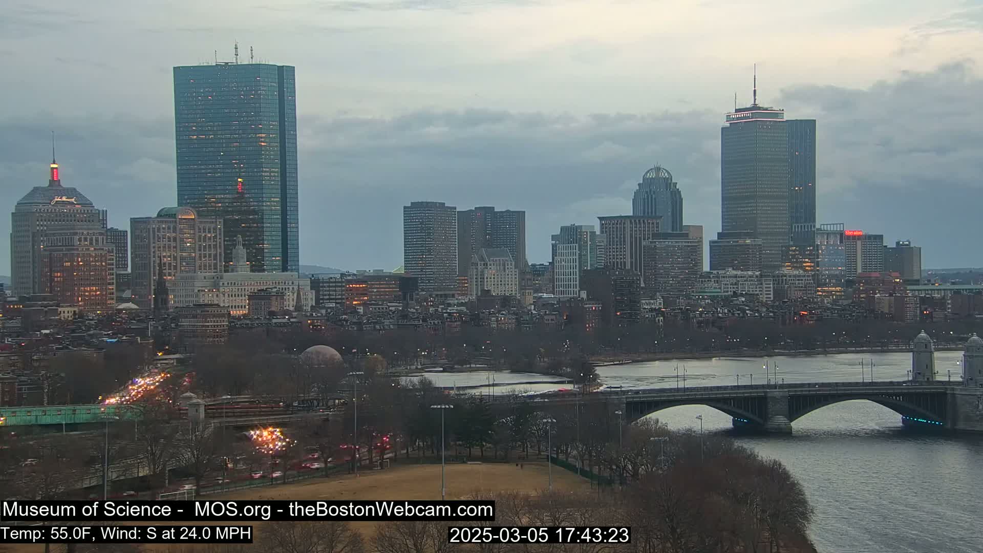 A cityscape with numerous skyscrapers and bridges is visible under an overcast sky, with a south wind at 24 mph.