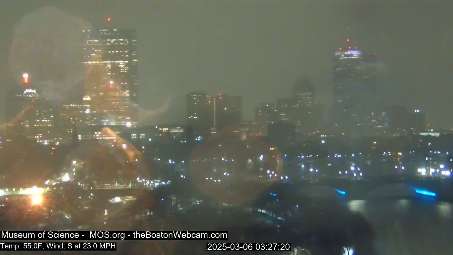 A nighttime view of a city skyline shrouded in hazy weather conditions, with numerous city lights visible.