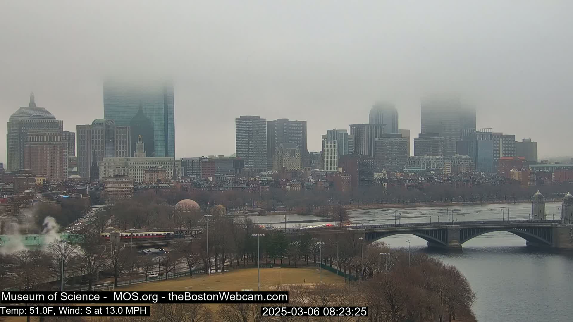 A foggy cityscape with a river and bridge is seen from a distance, with a south wind of 13 mph and a temperature of 51°F.