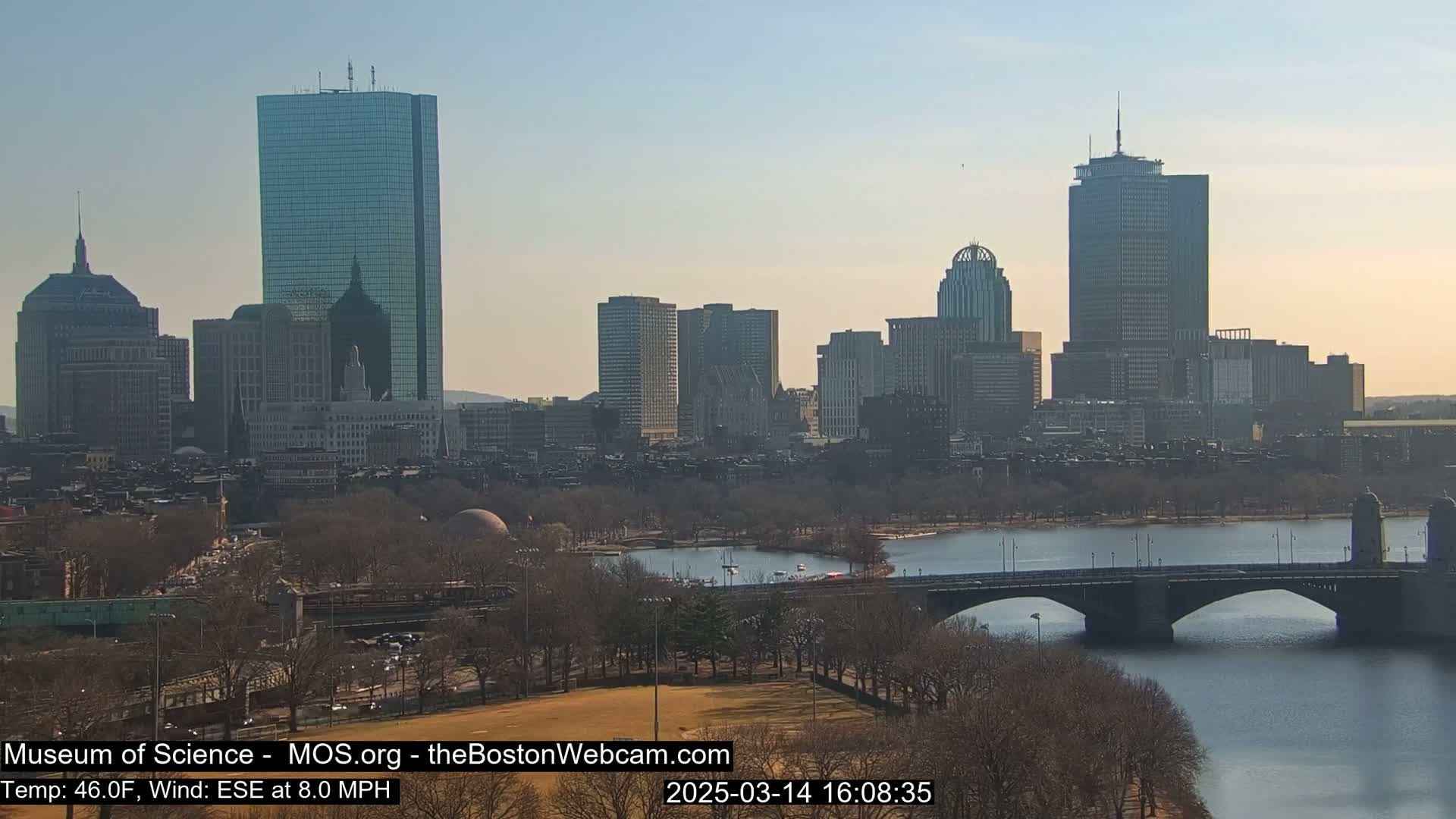 A cityscape with numerous skyscrapers and bridges is visible across a calm body of water under a clear, sunny sky.
