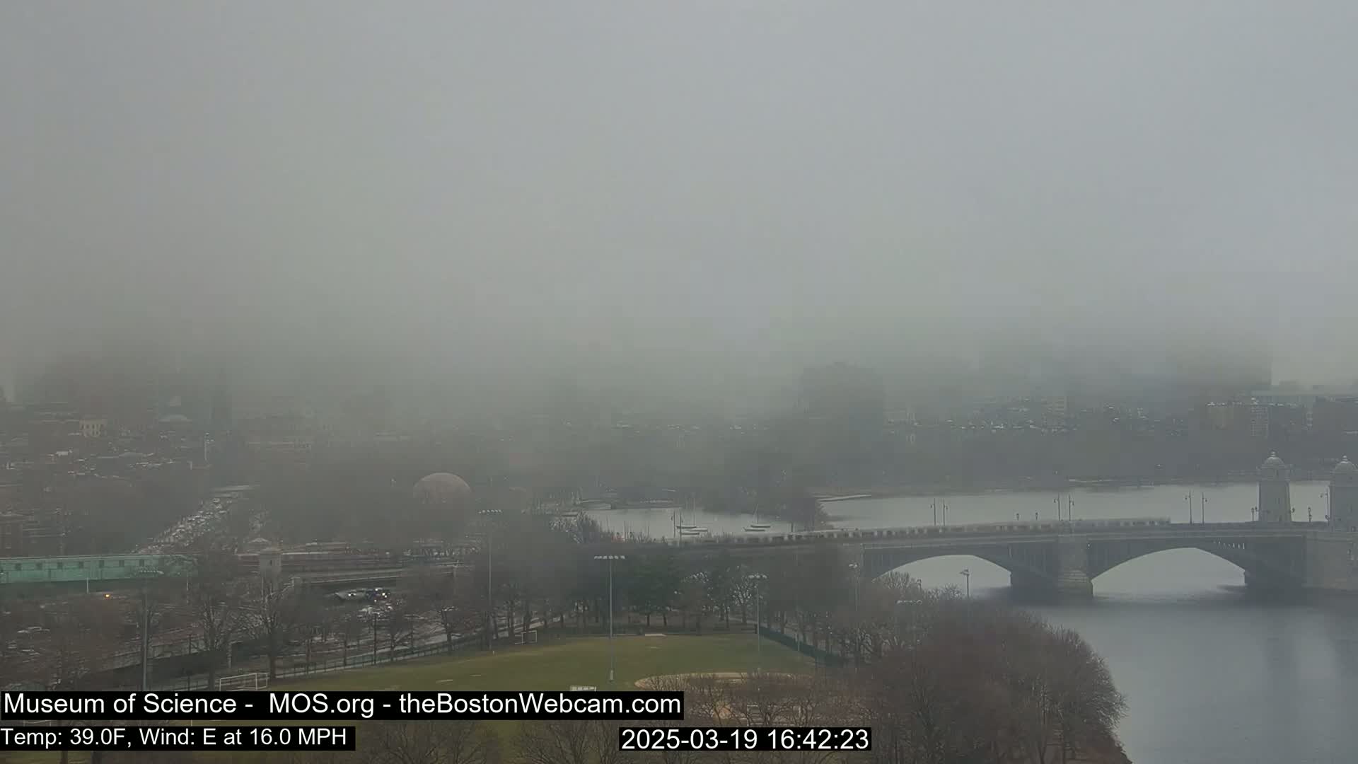 A foggy cityscape with a bridge spanning a river, viewed from an elevated vantage point.